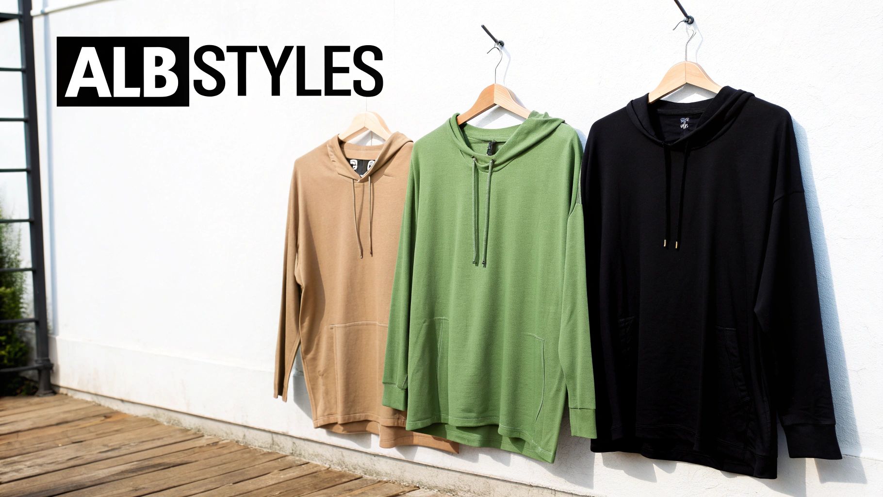 Three colorful hoodies in tan, green, and black from ALB Styles hanging on a white wall.