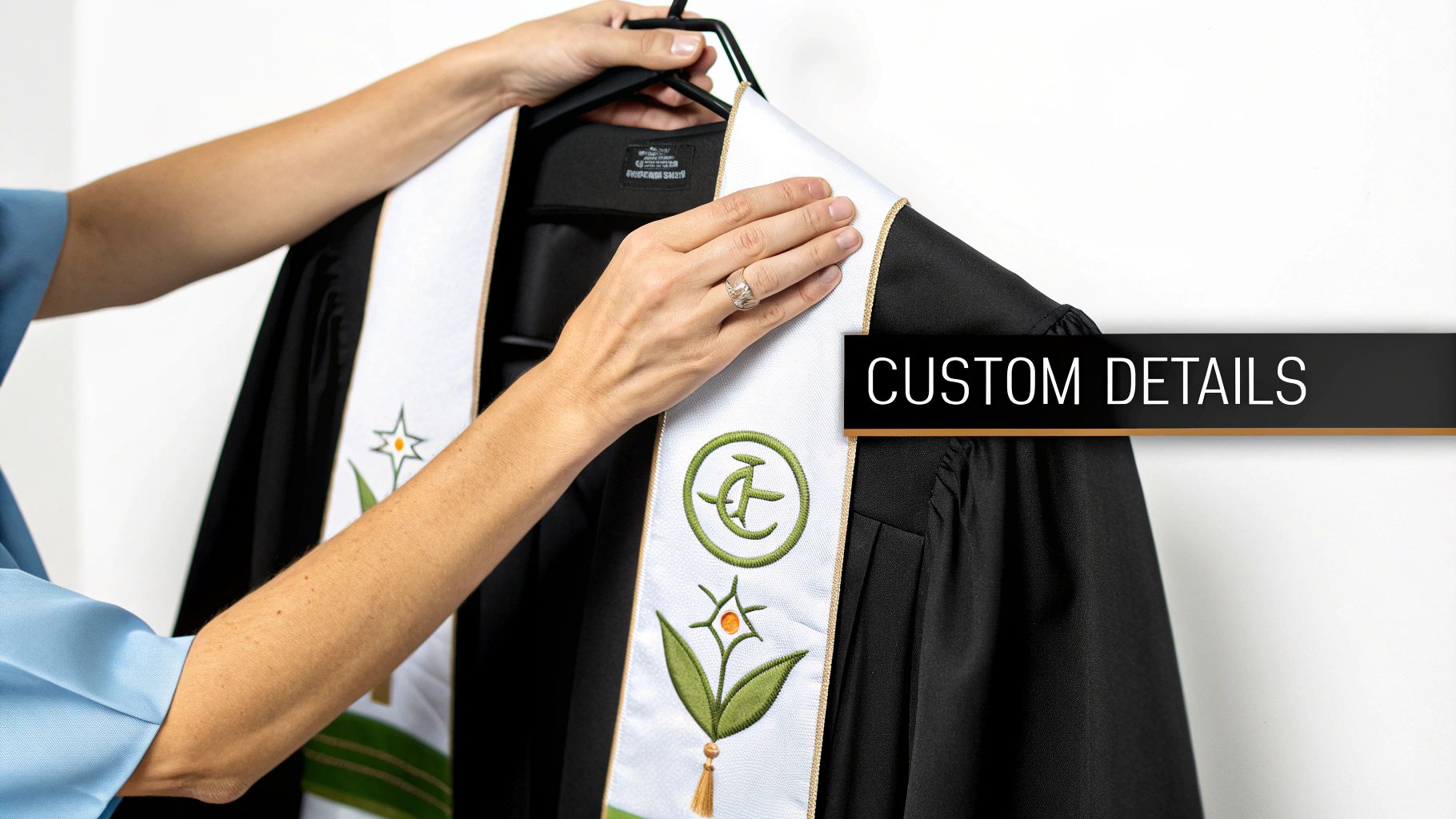 A person's hands adjust a black choir robe with an embroidered white stole featuring green patterns and tassels.