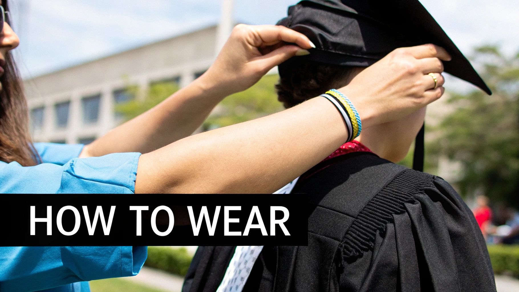 A person in a blue top adjusts a black graduation cap on another person wearing a gown outdoors.