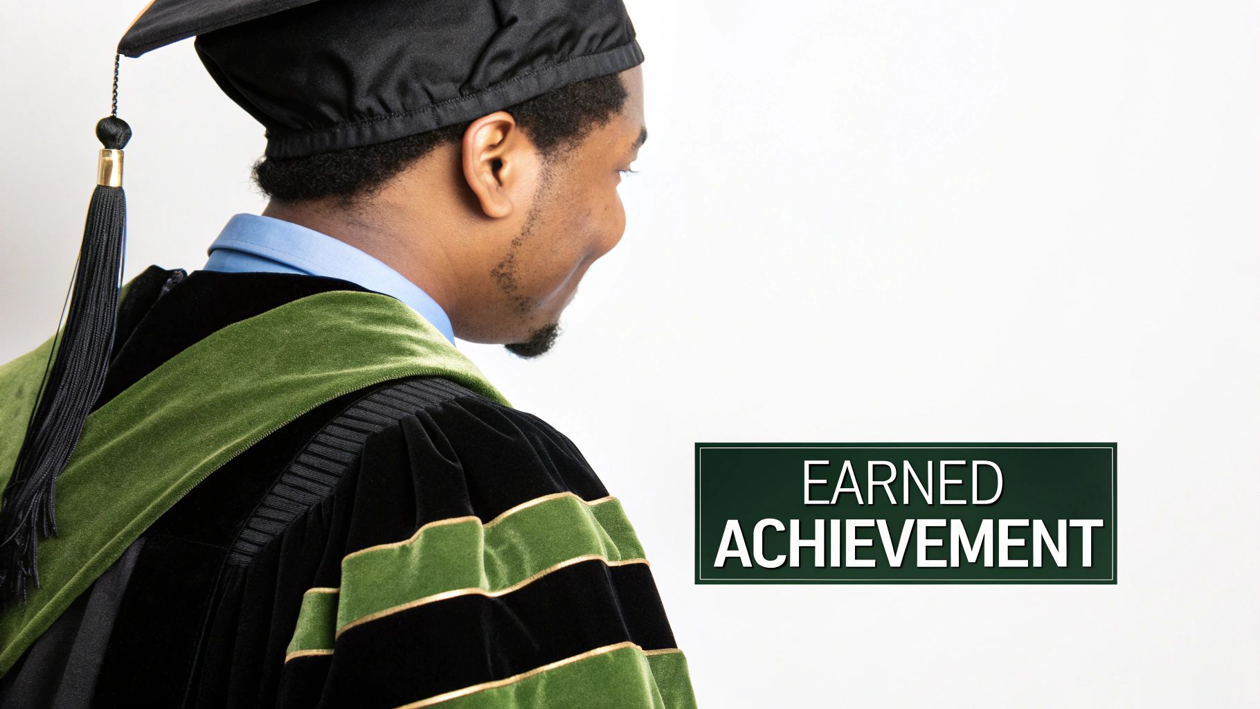 A graduate in a black and green doctoral cap and gown looks toward a sign saying 'EARNED ACHIEVEMENT'.