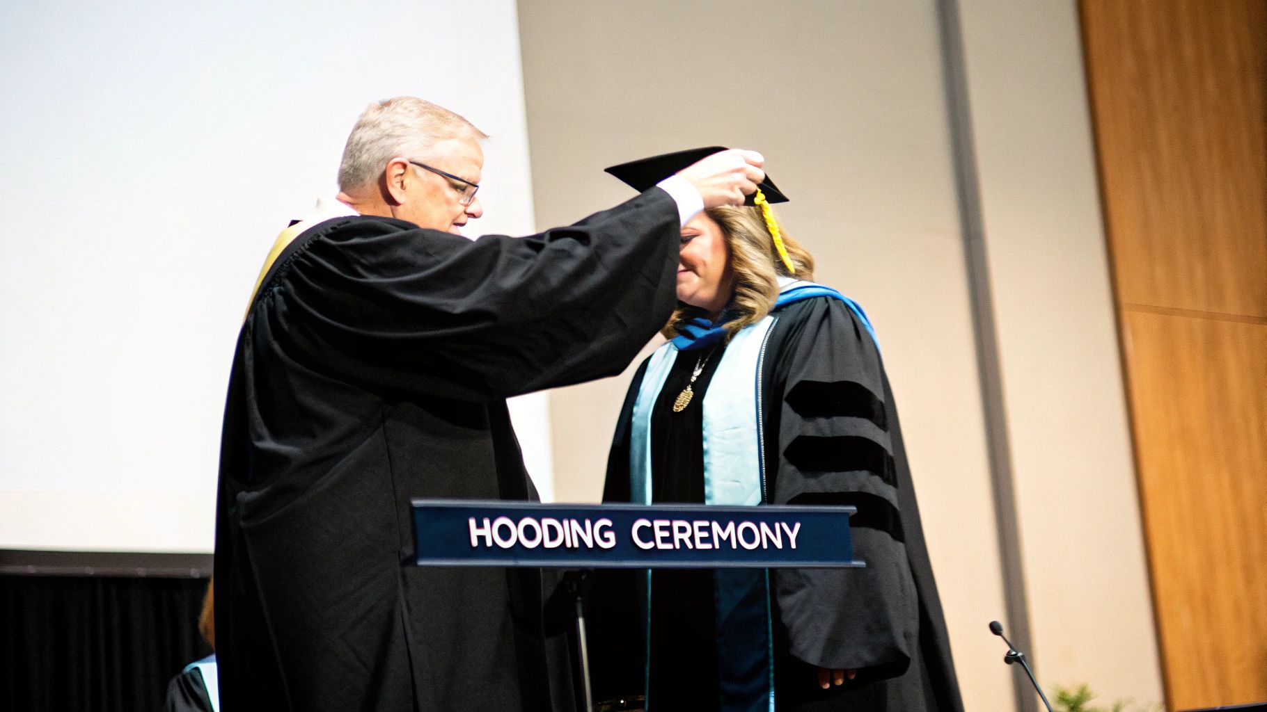 A graduate being hooded on stage by a faculty member during a ceremony.