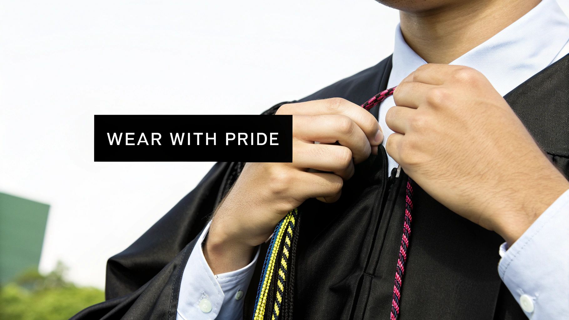 Close-up of a graduate in a black gown adjusting colorful honor cords with text 'WEAR WITH PRIDE'.