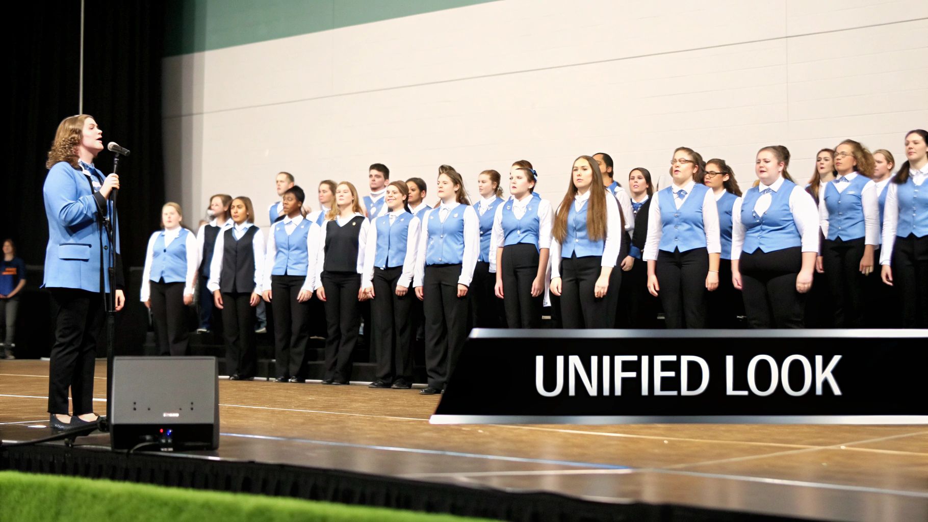 A choir performs on stage, with a female soloist singing into a microphone, and members in matching blue vests.