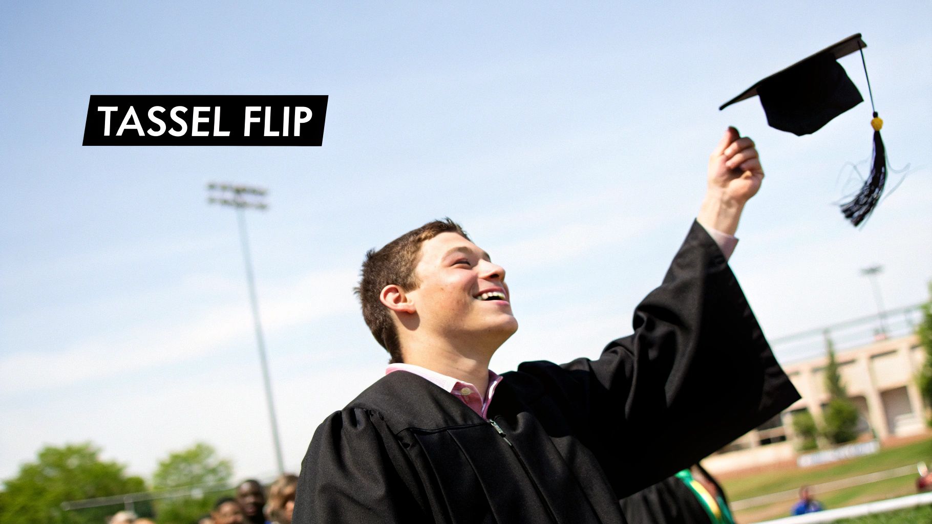 A joyful graduate in a black gown smiles, looking up while flipping their cap and tassel.