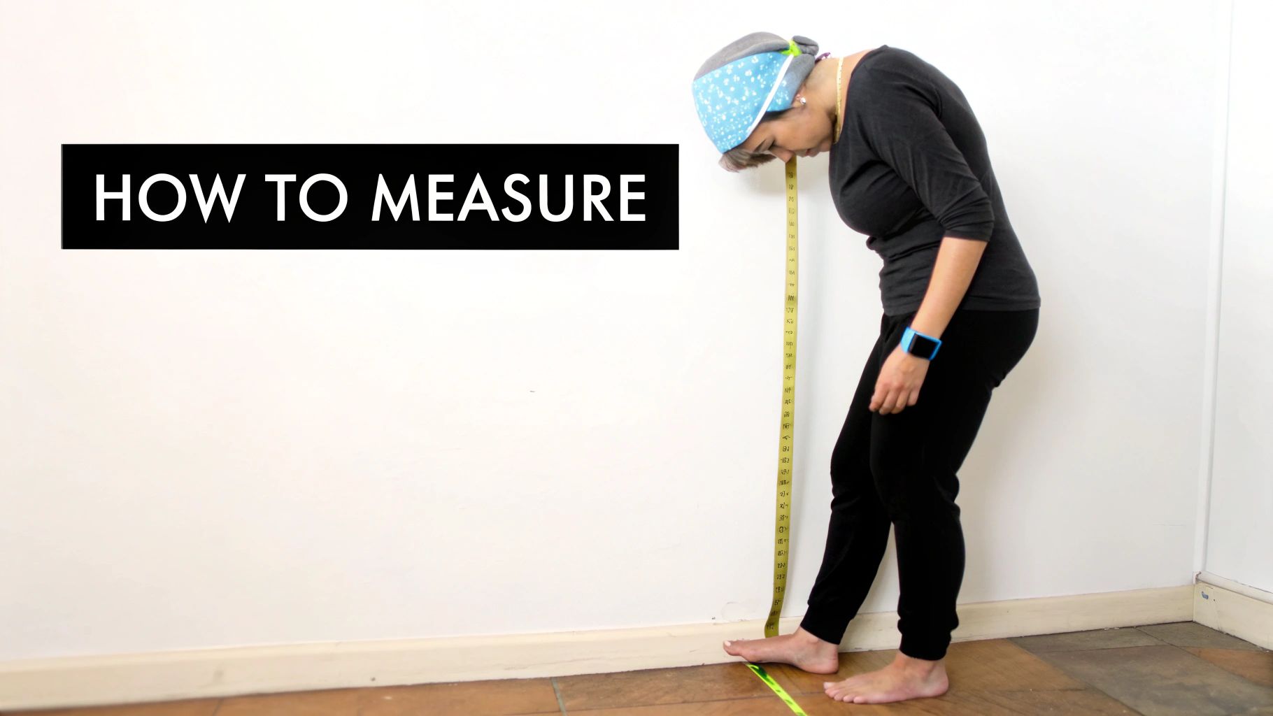 A person measures their height against a white wall using a yellow measuring tape.