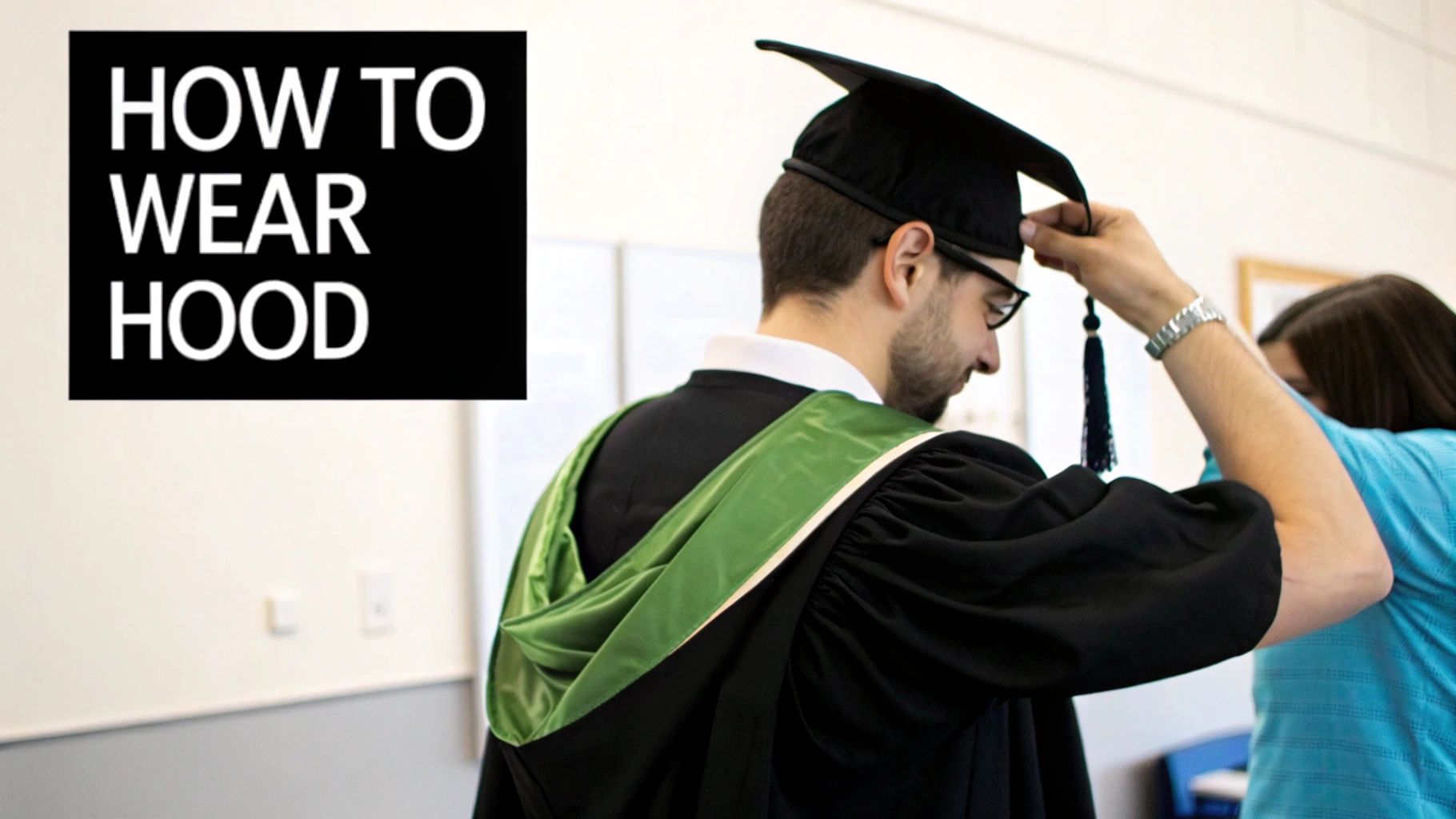 A graduate in a black gown and green hood being helped to adjust their graduation cap and tassel.