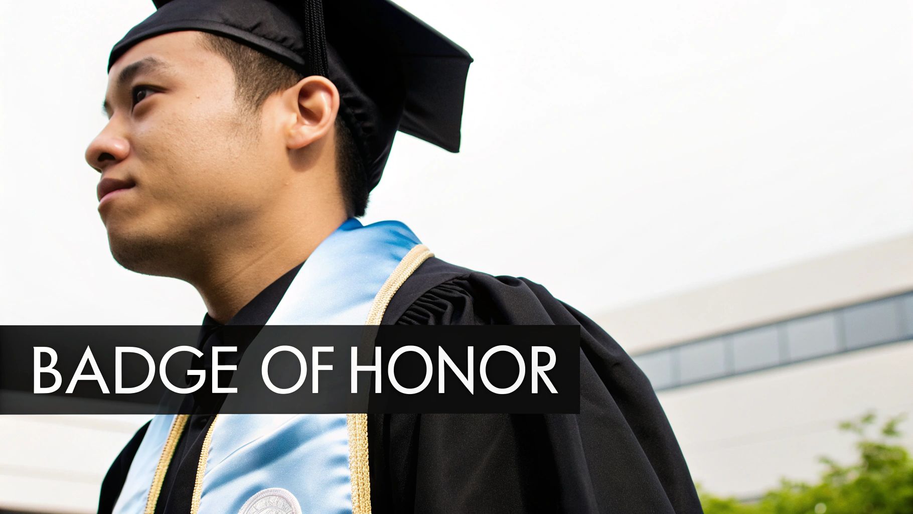A graduating student in a black cap and gown, wearing a light blue satin stole, looking thoughtfully to the side.