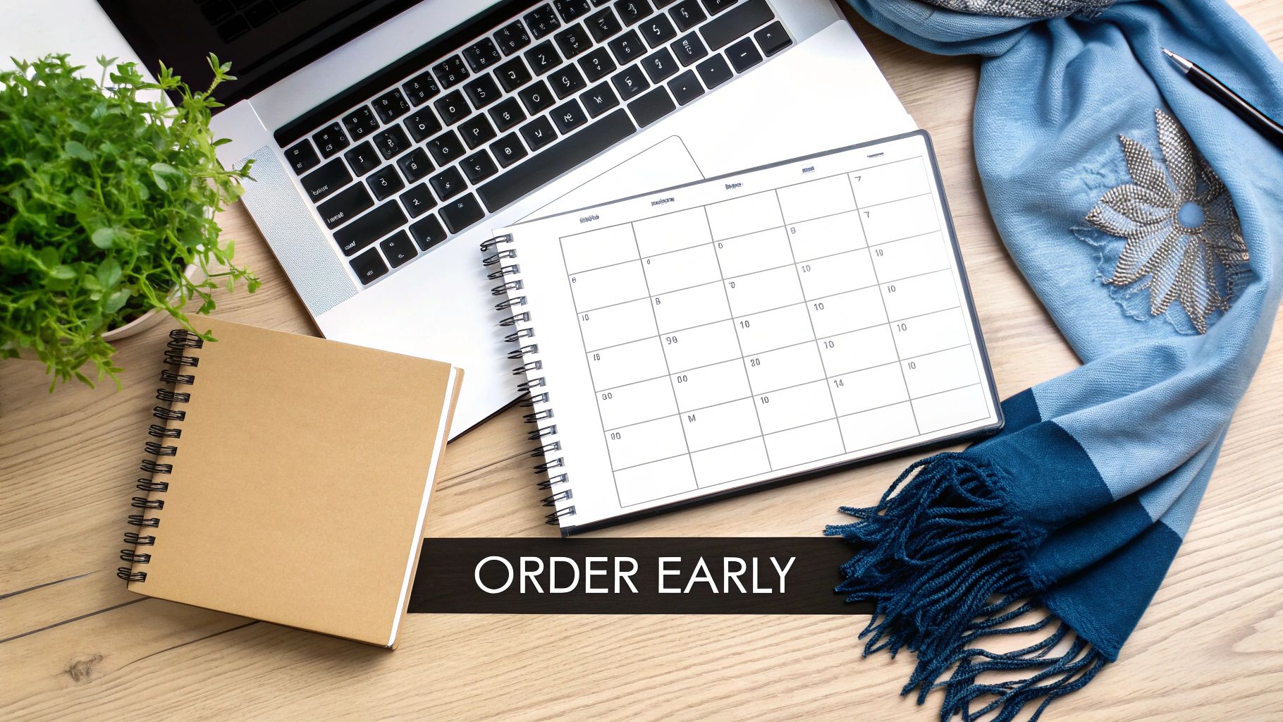 A flat lay of a desk with a laptop, green plant, notebook, calendar, blue scarf, and 'ORDER EARLY' text.