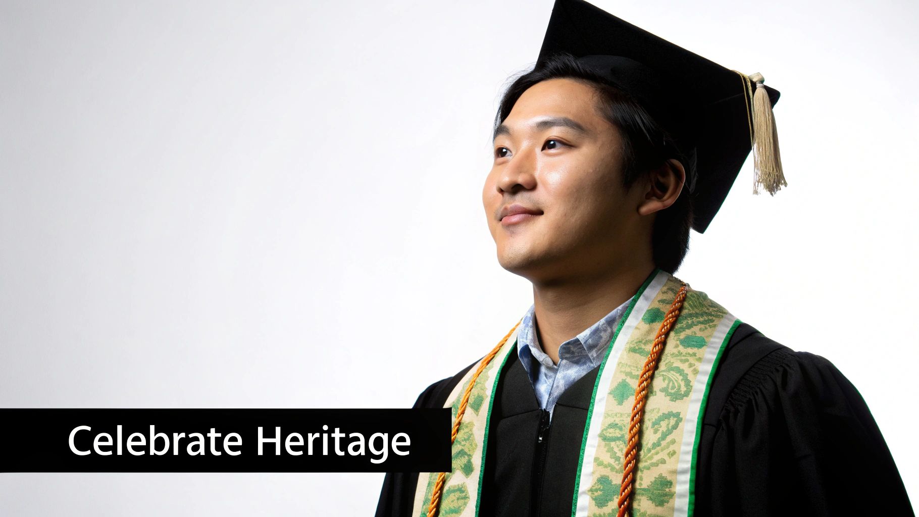 A young Asian man in graduation cap and gown with a heritage stole and cords, looking optimistically.