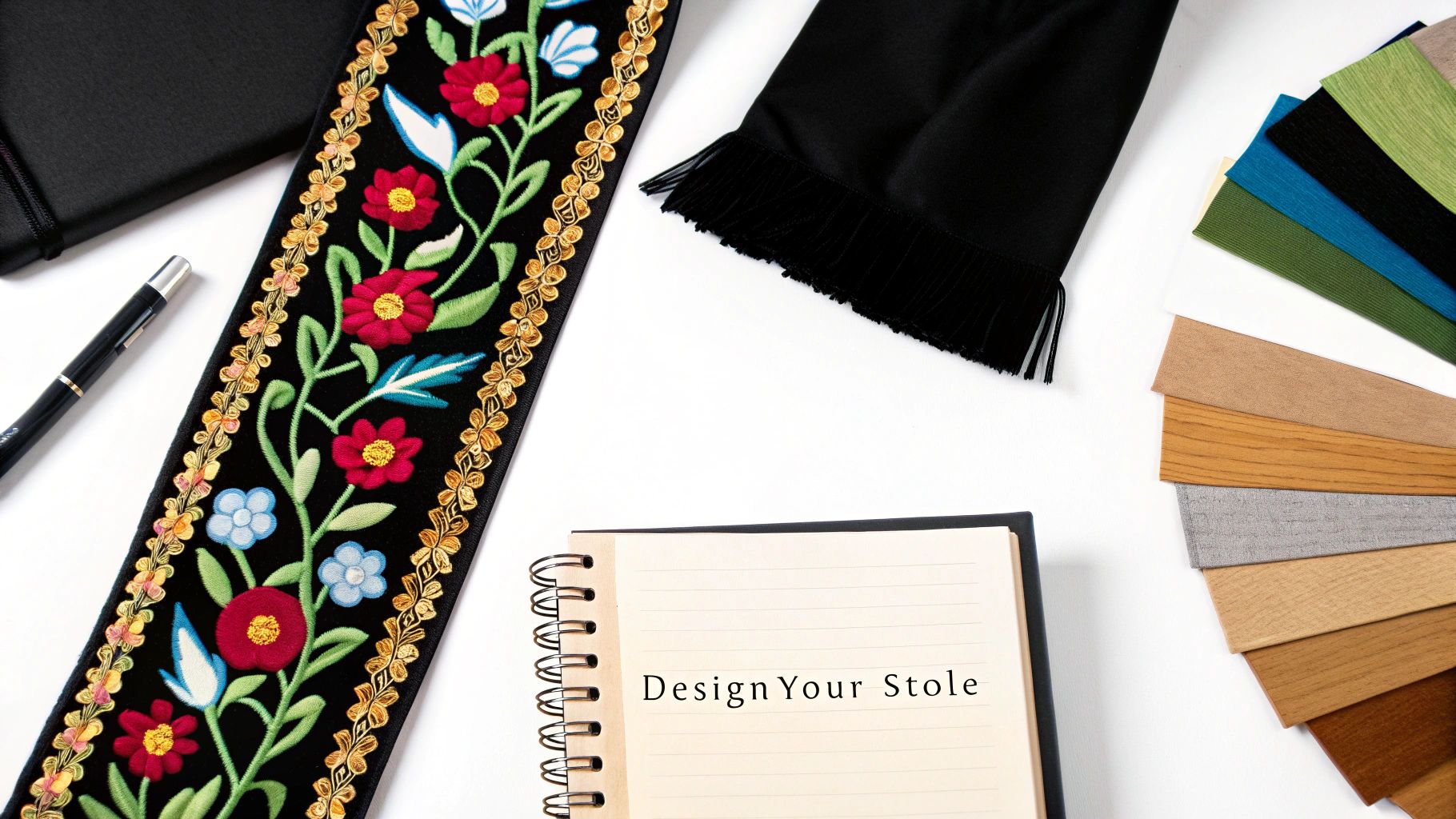 A vibrant embroidered black stole, 'Design Your Stole' notebook, pen, and colorful fabric swatches on white.