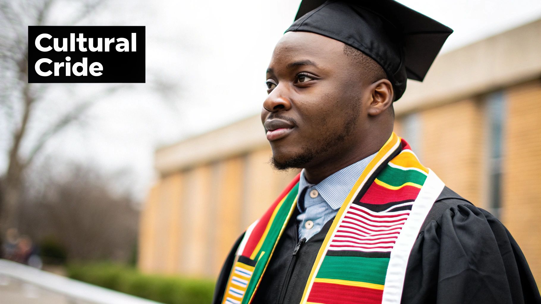 A proud Black graduate in cap, gown, and colorful cultural stole looks forward.