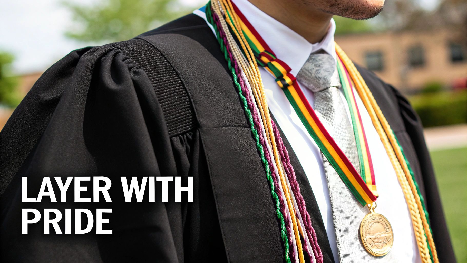A proud graduate in a black gown, white shirt, and tie, adorned with colorful graduation cords and a medal.