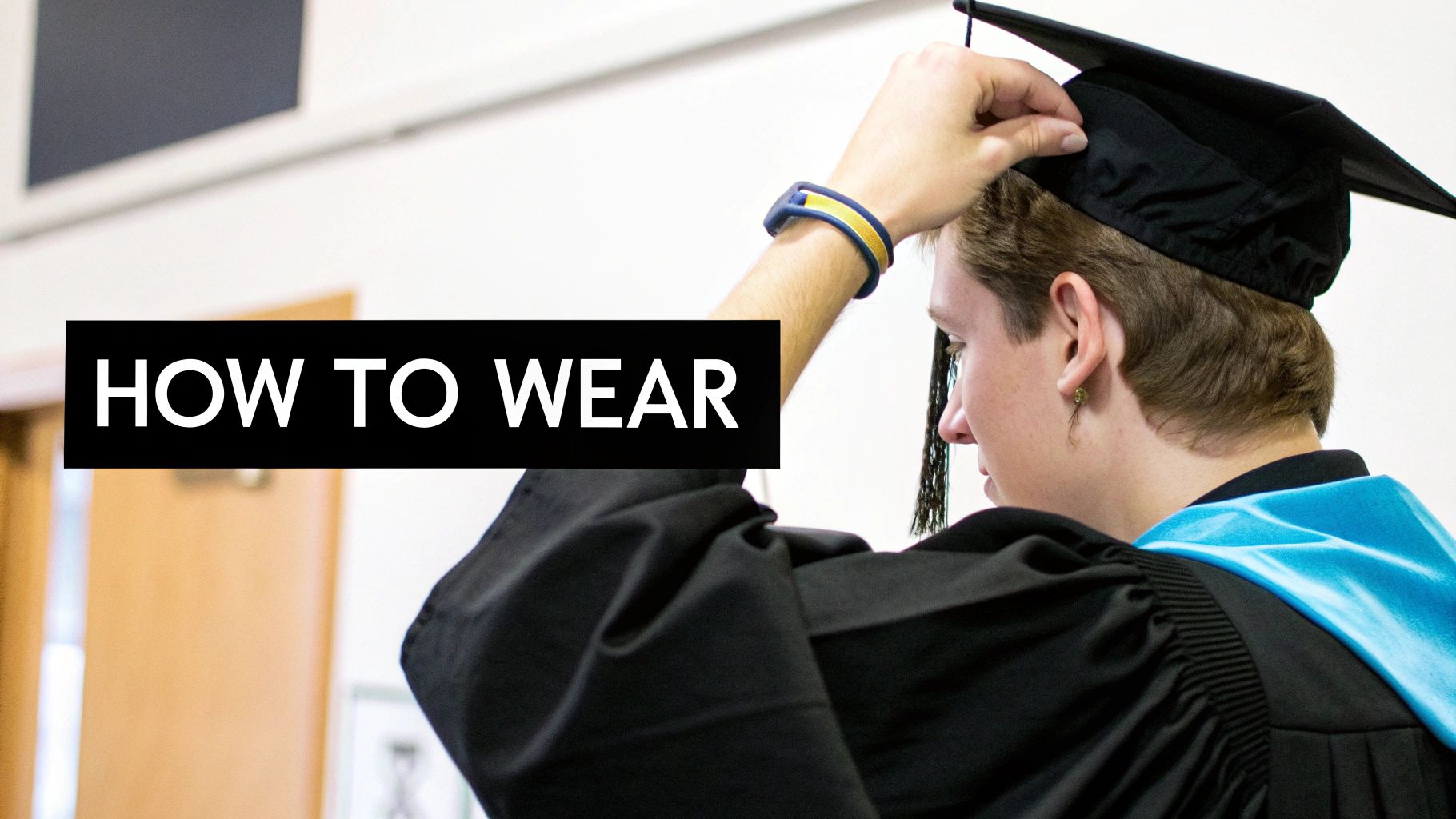 A person in a black graduation gown and cap, adjusting the cap, with a blue hood.