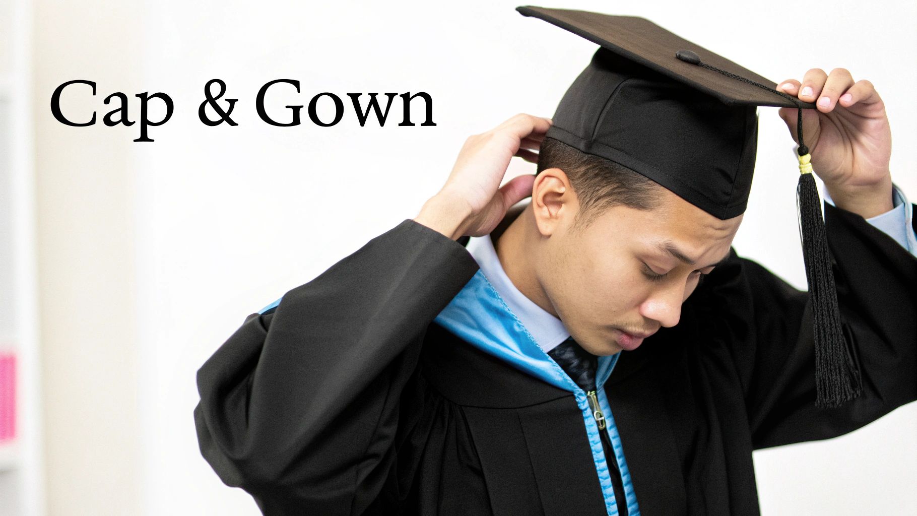 A graduate in a black gown and blue stole adjusts his black graduation cap with a tassel.