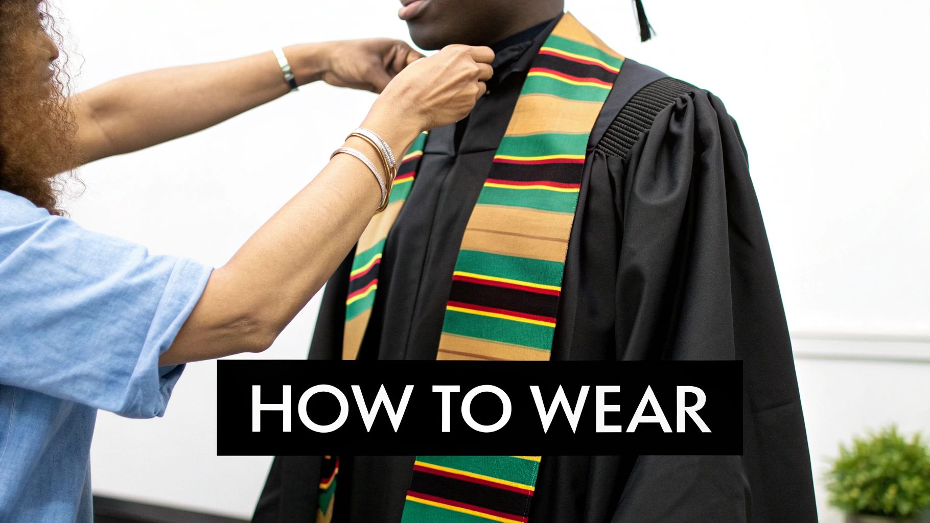 A person adjusts a colorful Kente stole on a graduate wearing a black cap and gown, demonstrating how to wear it.