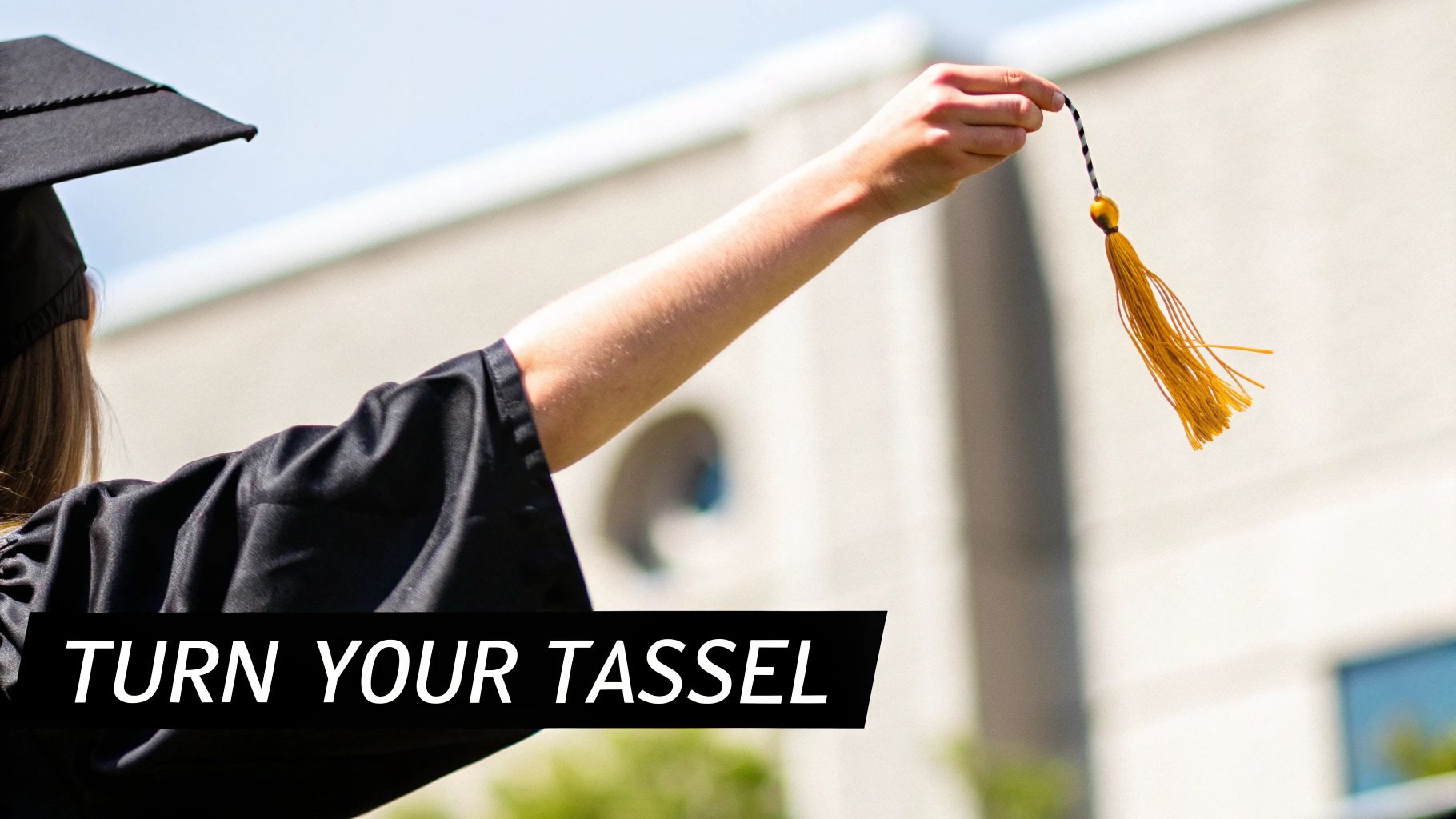 A graduate in a black cap and gown holds up a yellow tassel against a bright sky, ready to turn it.
