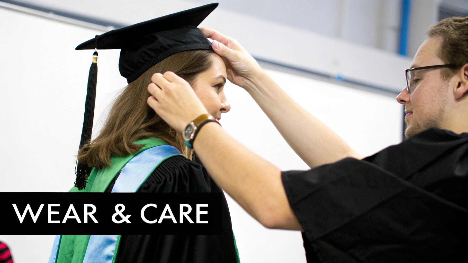 A person helps adjust a graduate's black cap and gown with a green and blue stole.