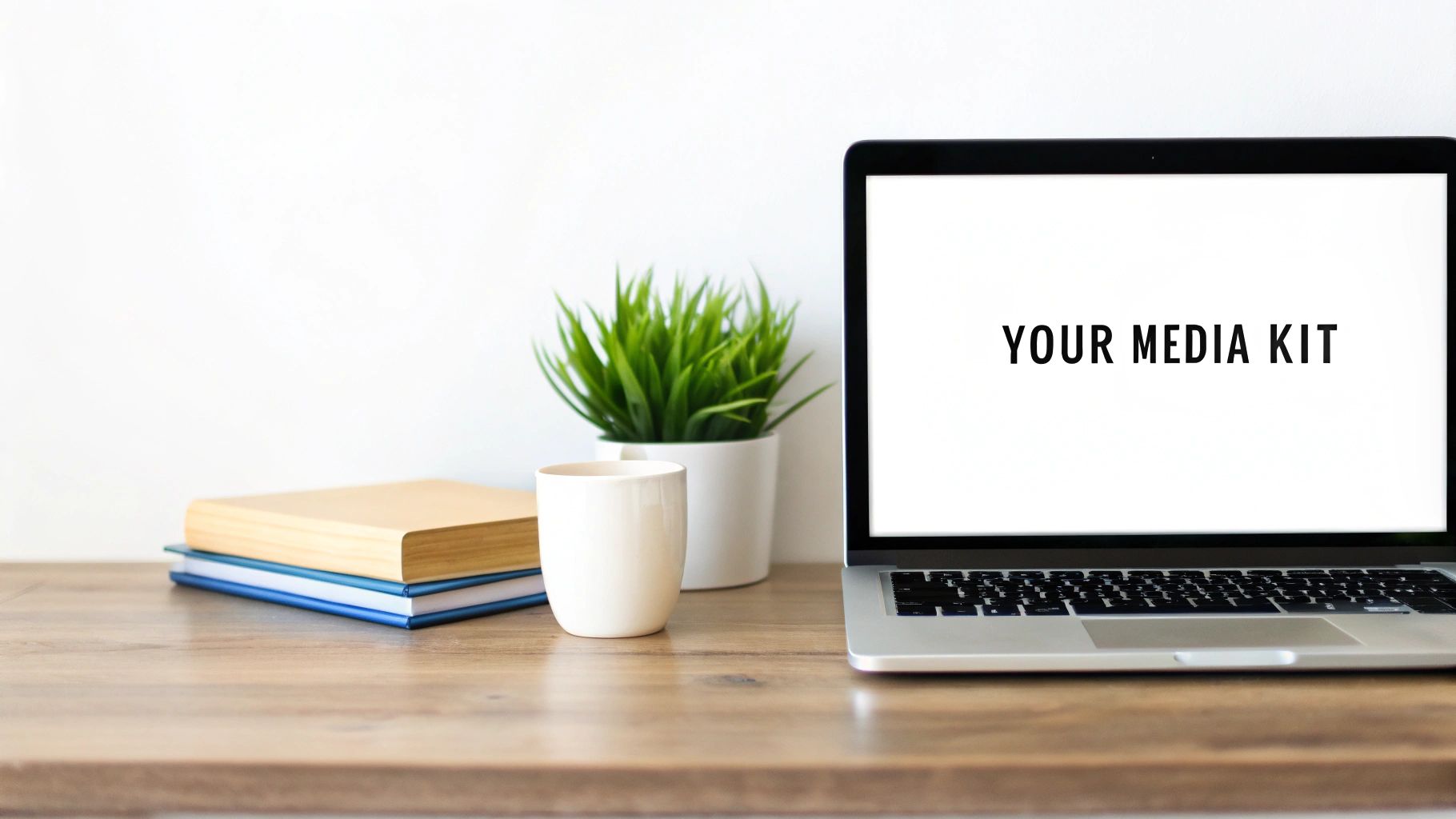 White workspace with a laptop showing 'YOUR MEDIA KIT', books, a mug, and a green plant.