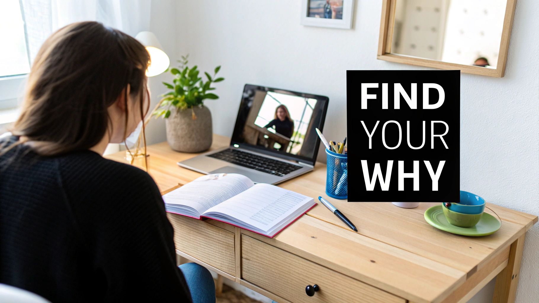 A person works at a wooden desk with a laptop showing a video call, an open notebook, and a 'Find Your Why' sign.