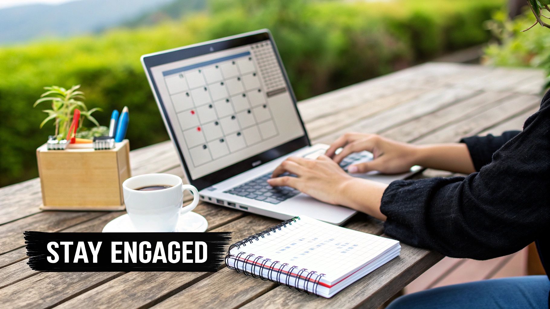 Person typing on a laptop outdoors with a calendar screen, coffee, and notebook on a wooden table.