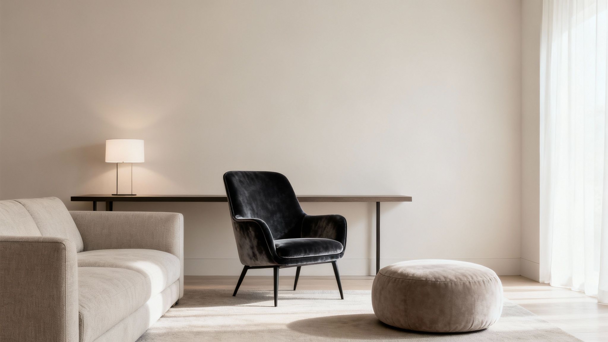 A minimalist living room with a beige sofa, dark velvet accent chair, and console table with lamp.