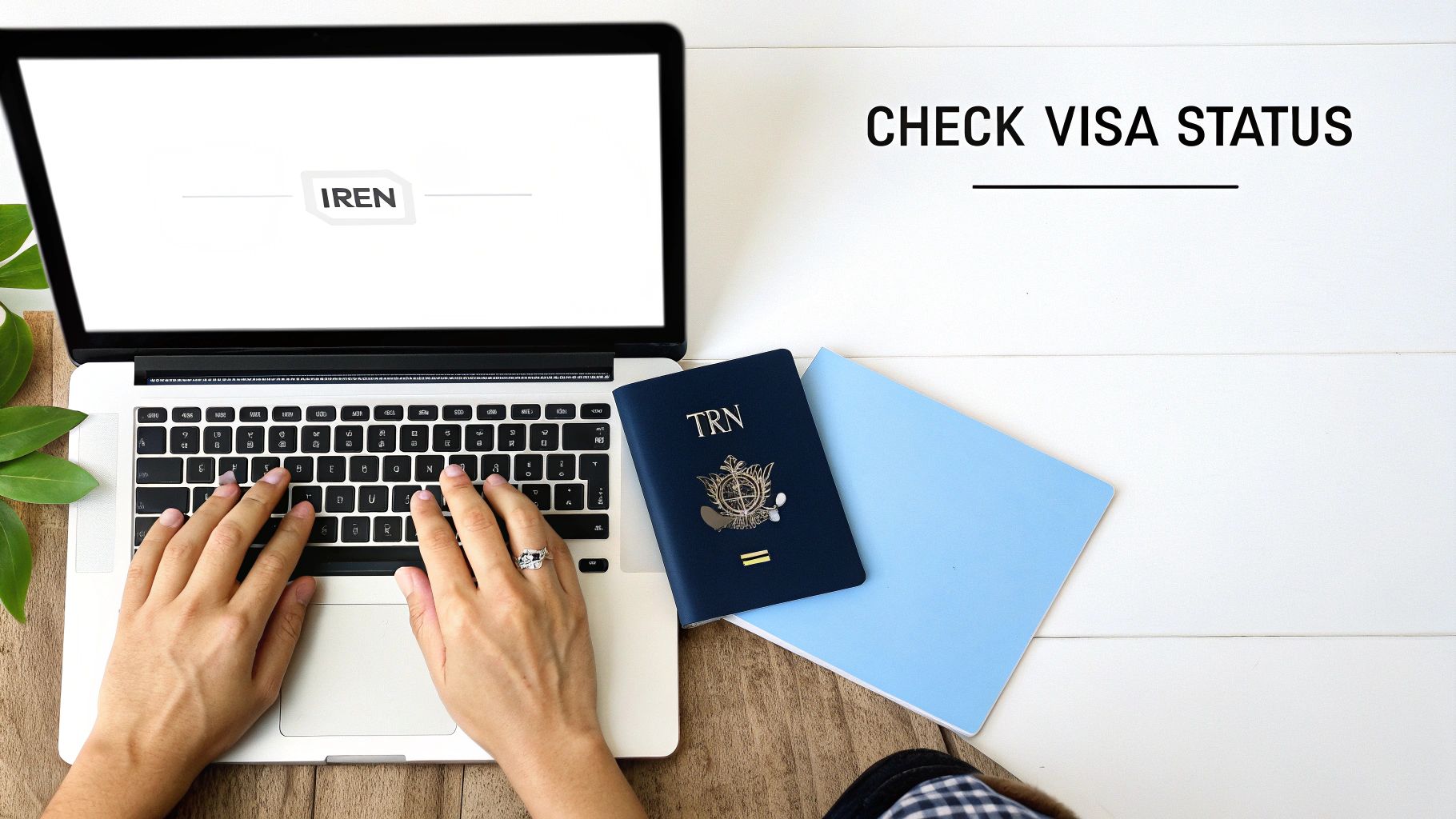 Person typing on a laptop to check visa status, with a passport and a blue notebook.