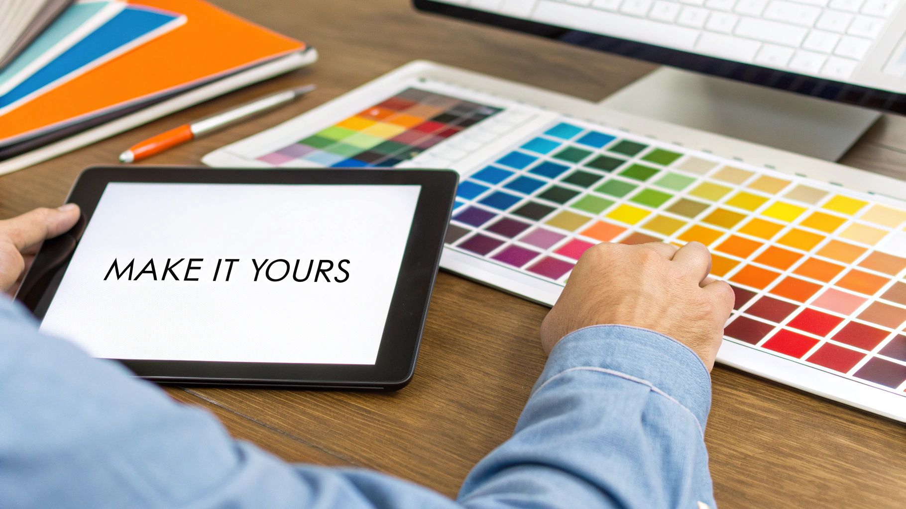 A person holds a tablet with 'MAKE IT YOURS' on screen, surrounded by color palettes, suggesting design work.