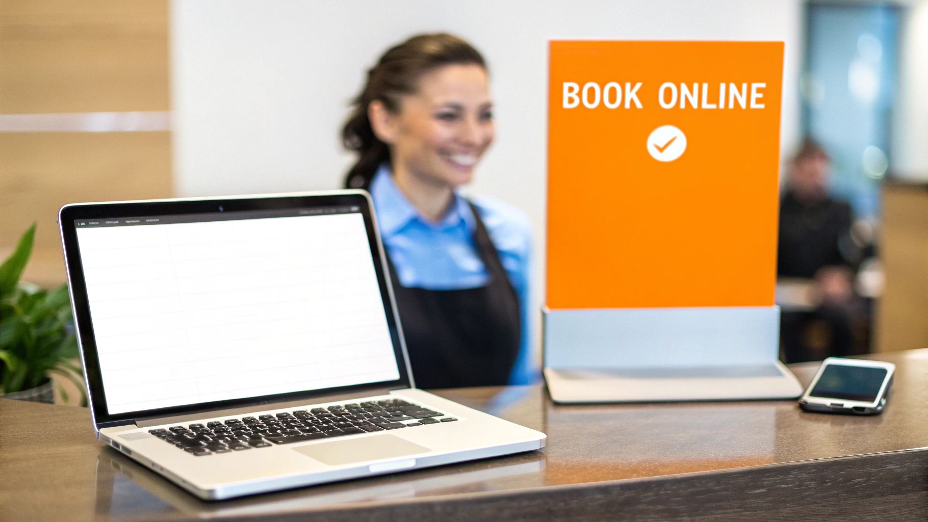 Reception desk with a laptop, smartphone, and 'BOOK ONLINE' sign, featuring a smiling attendant.