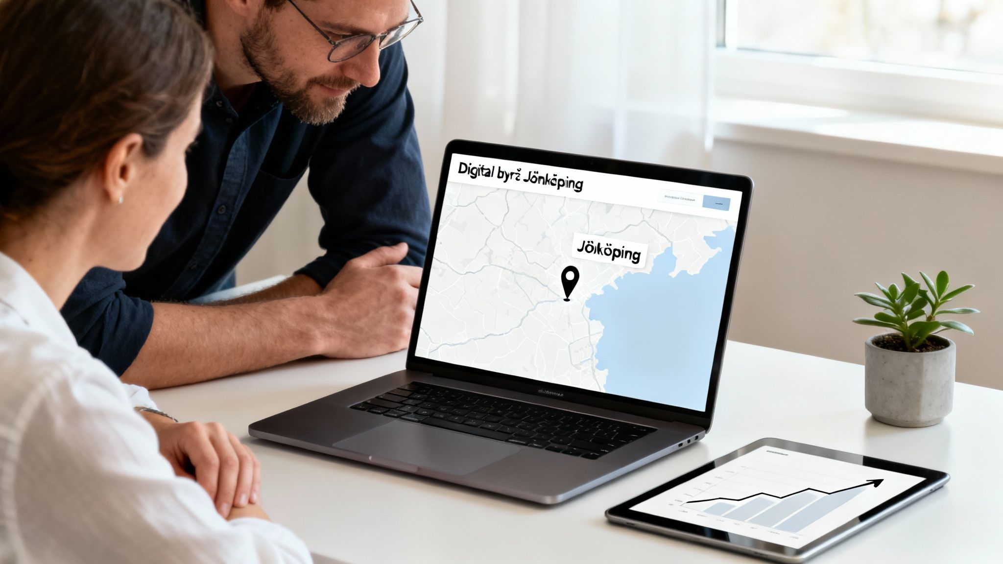 Två personer tittar på en laptop som visar en karta över Jönköping och texten 'Digital byrå Jönköping'. En surfplatta med en graf ligger bredvid.