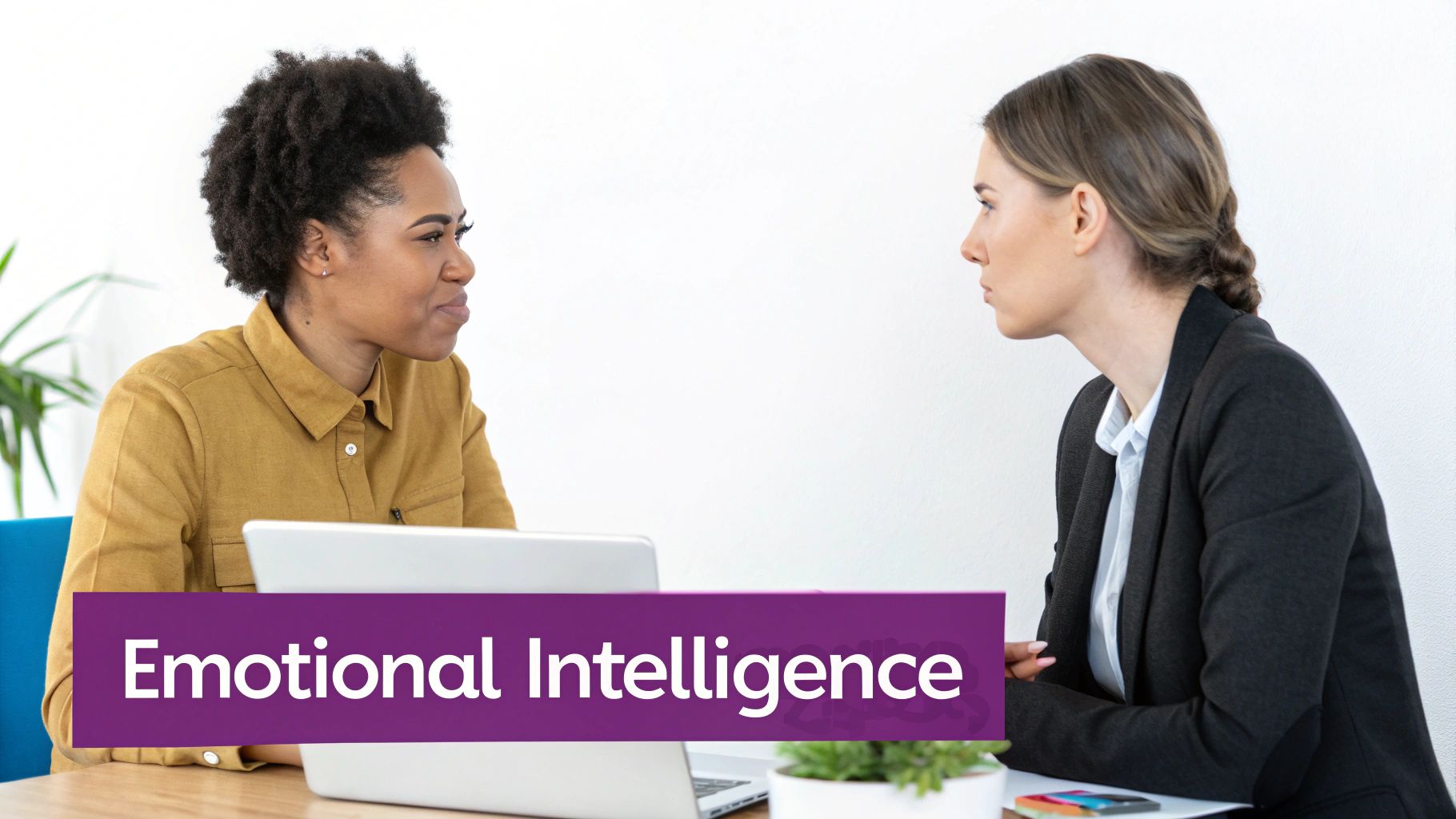 Two women engaged in conversation at a desk with laptops, discussing emotional intelligence.
