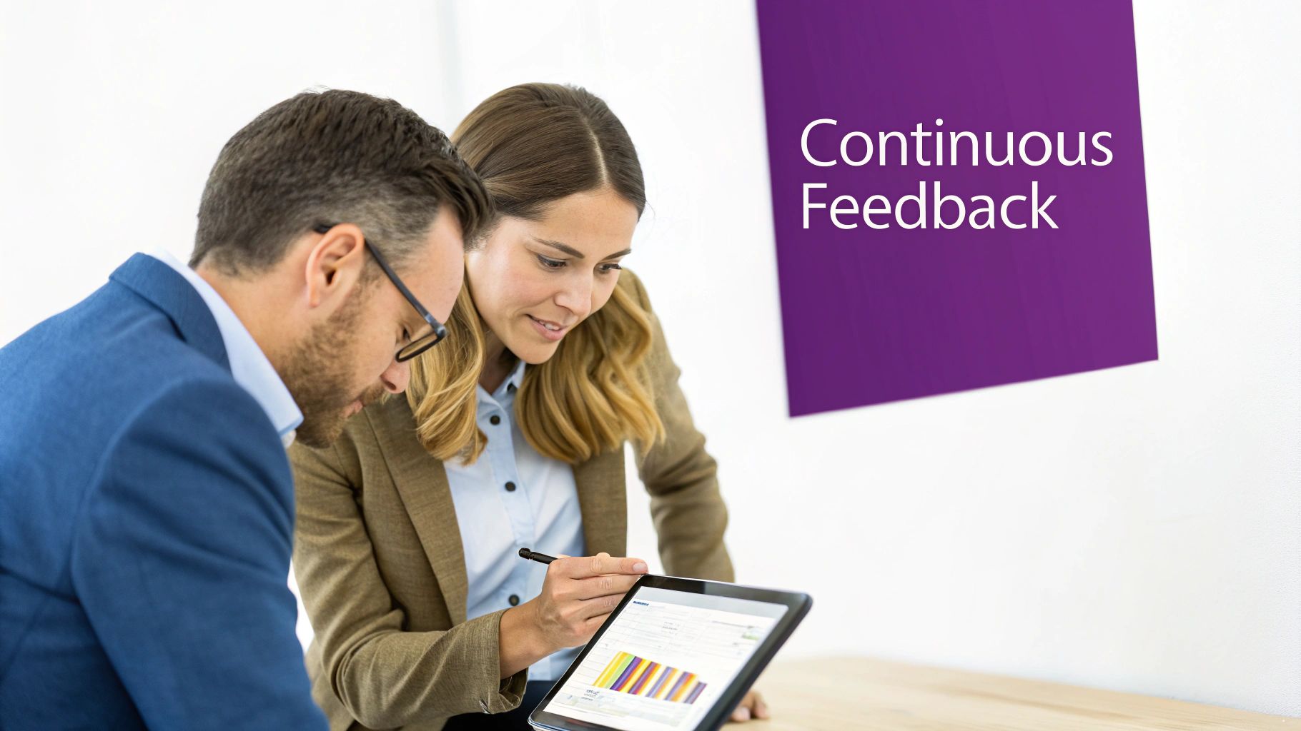 Two business professionals discussing data on a tablet, with 'Continuous Feedback' displayed on a wall.
