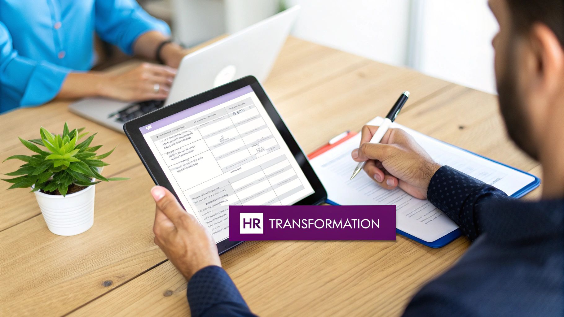 Professionals collaborating at a desk, utilizing a laptop, tablet, and documents for HR transformation initiatives.
