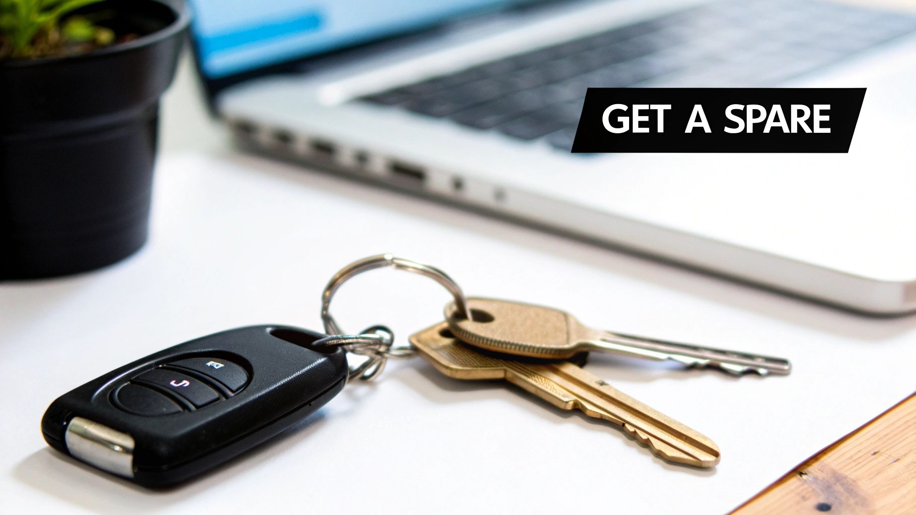 Car keys on a desk next to a laptop, with a black banner saying 'GET A SPARE'.