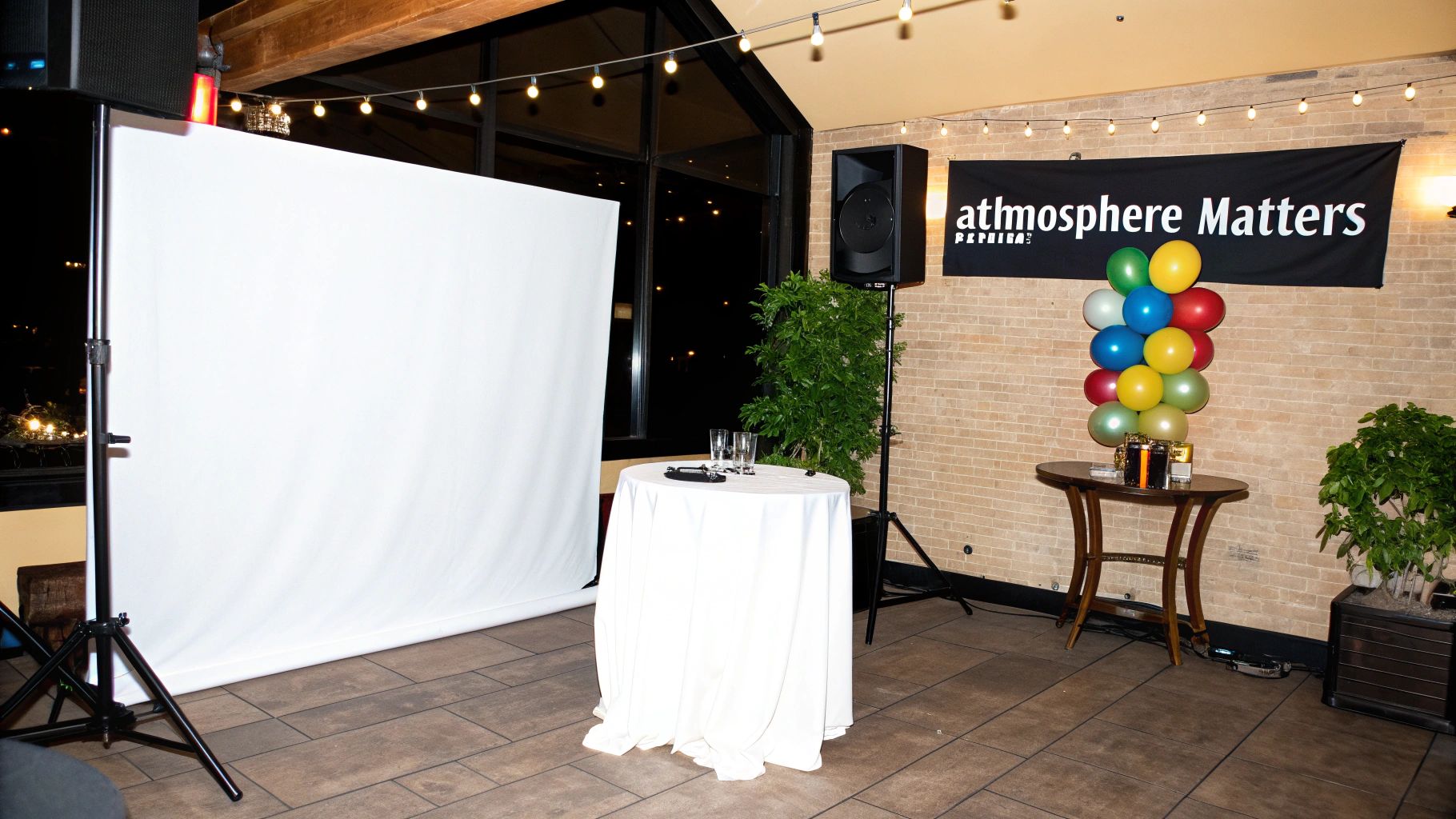 A room set up for an event, featuring a large screen, speaker, colorful balloons, and an 'atmosphere Matters' banner.