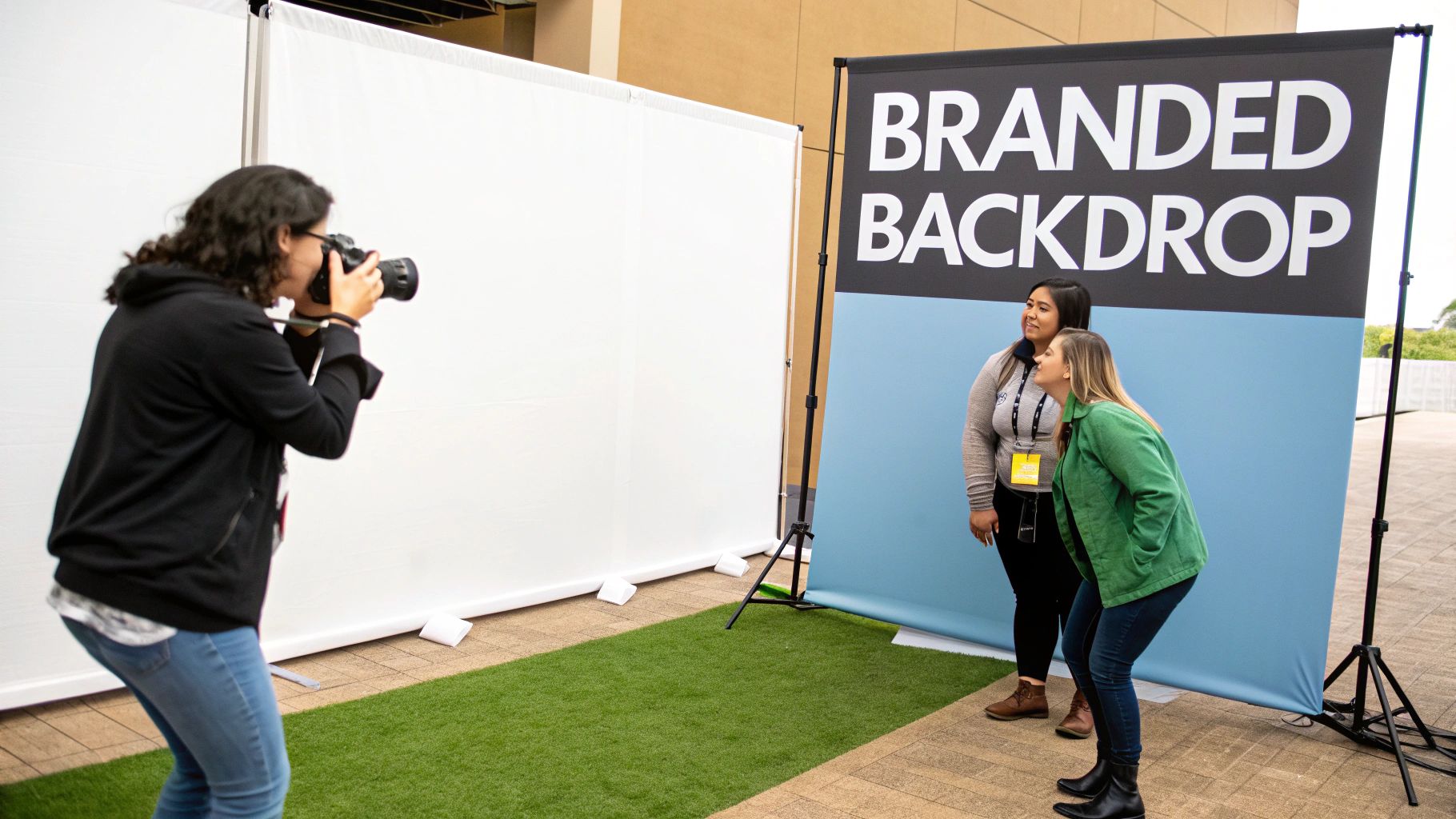 A photographer takes pictures of two women posing by a "Branded Backdrop" at an event.