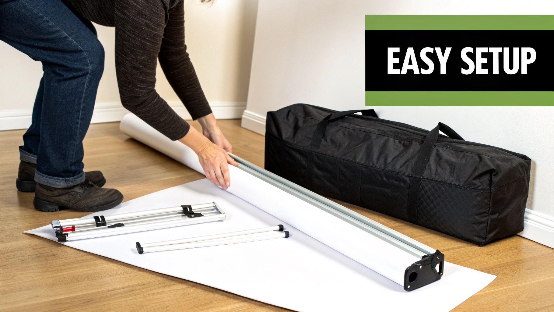 A person setting up a white banner or display on a wooden floor, with frame parts and a carrying bag nearby.