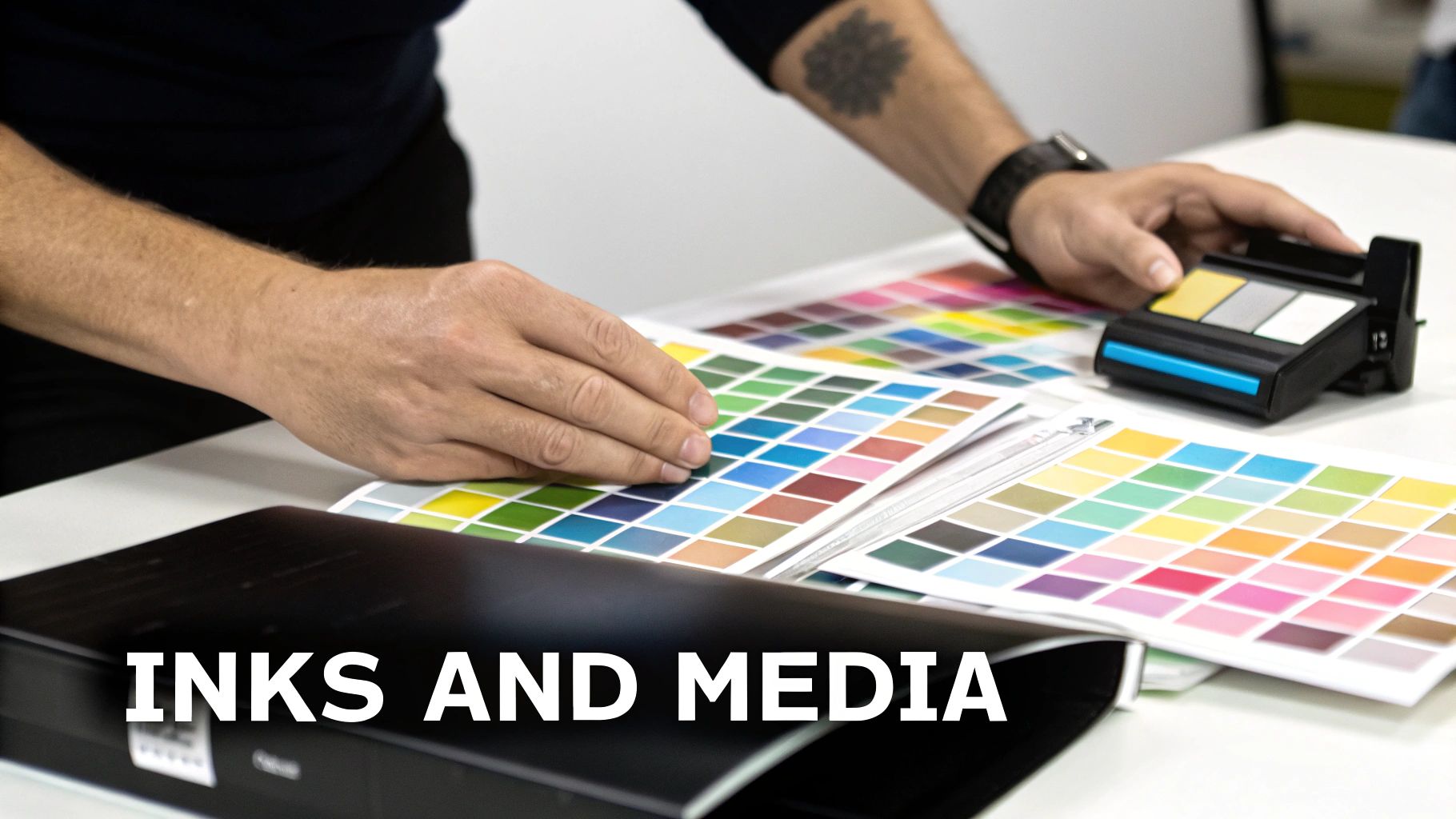 A person's hands reviewing colorful ink swatches and using a color measurement device on a white table.