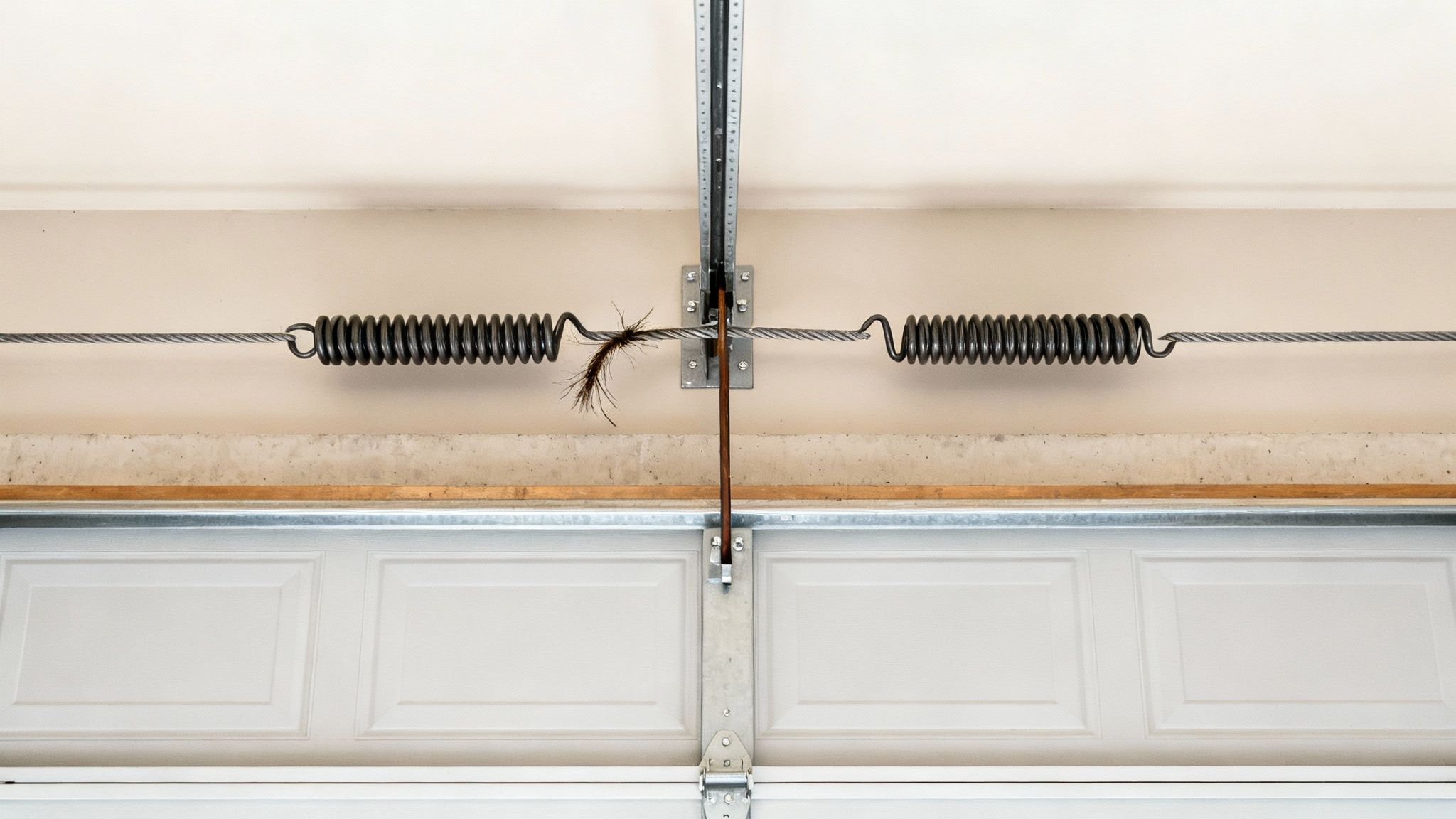 Close-up of garage door extension springs, cables, and central mechanism with hanging debris.