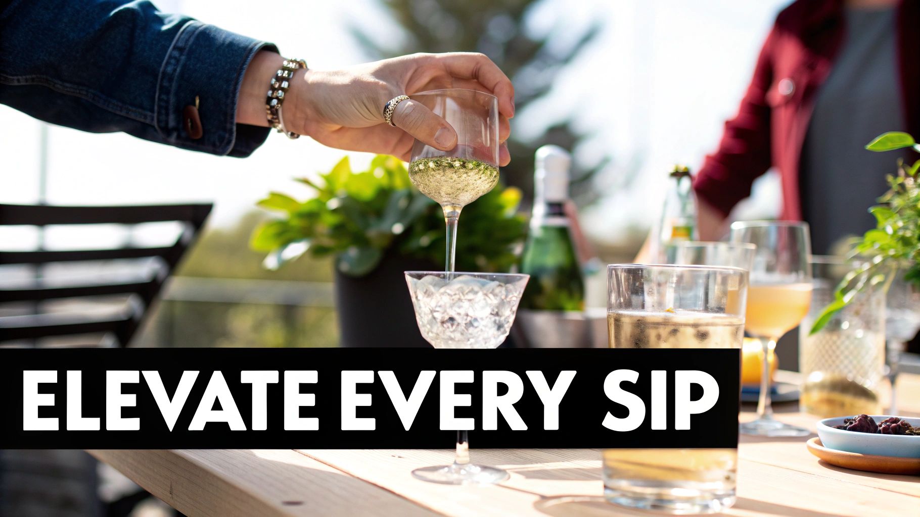 A hand pours sparkling wine into a glass during an outdoor gathering with various drinks and snacks.