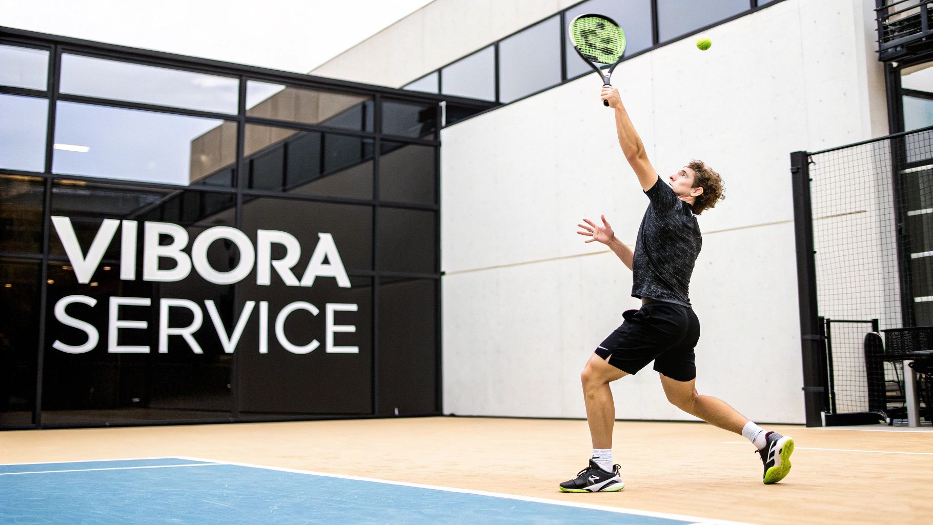 Jonge man serveert tijdens een padelwedstrijd op een buitenbaan met 'VIBORA SERVICE' op de achtergrond.