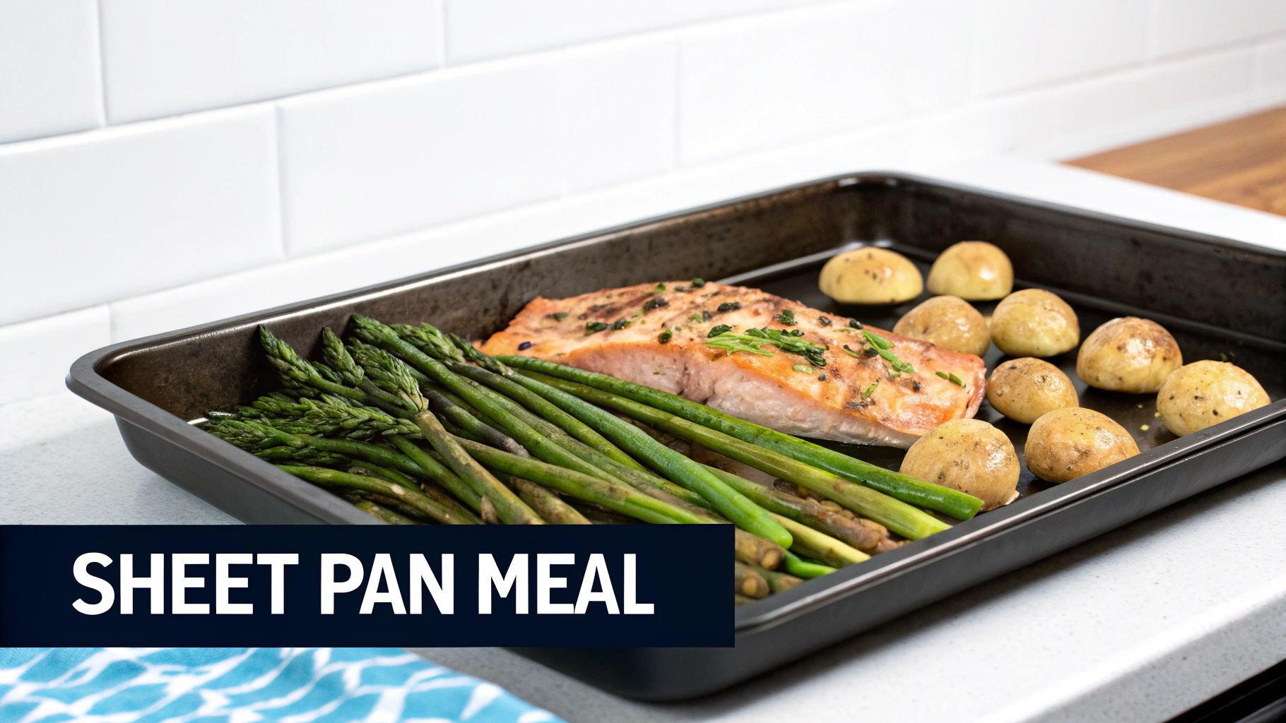 A healthy sheet pan meal with baked salmon, fresh asparagus, and roasted baby potatoes on a white counter.