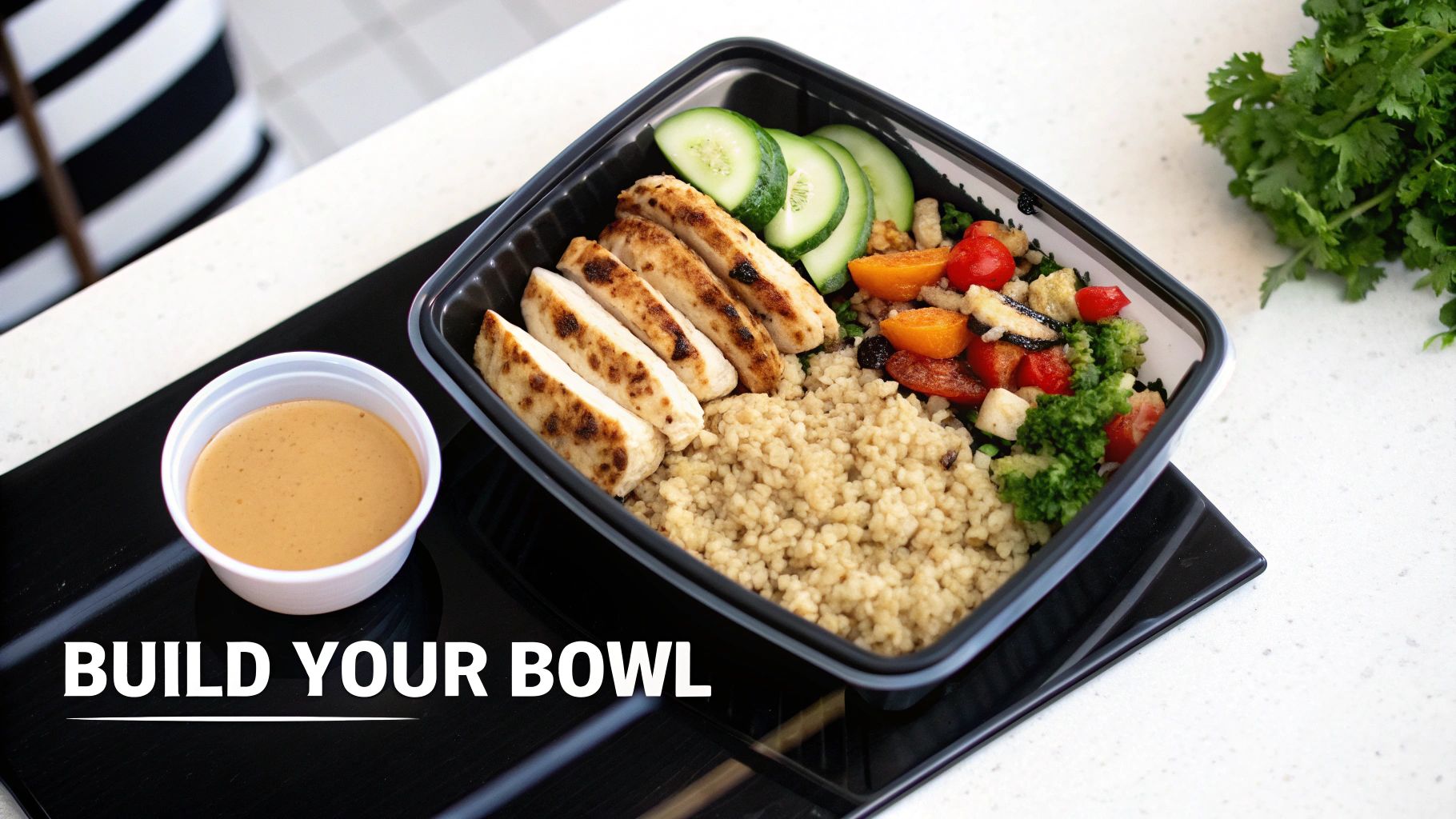 A healthy meal prep bowl with grilled chicken, grains, fresh vegetables, and a side of sauce.