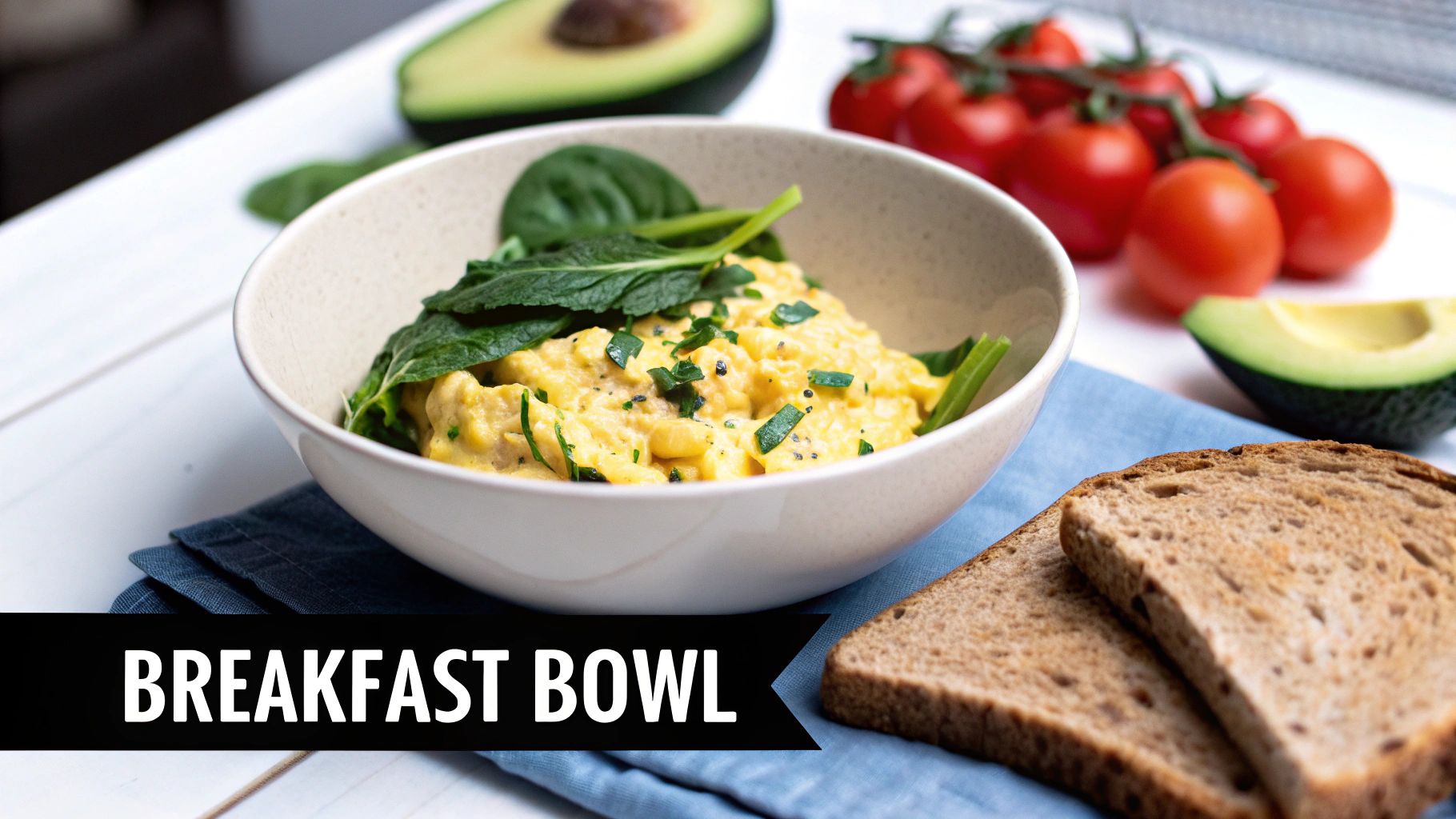 A healthy breakfast bowl with scrambled eggs, spinach, avocado, tomatoes, and whole-grain toast on a white table.