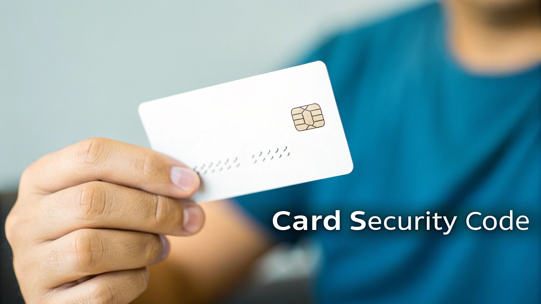 A person's hand holds a white credit card with an EMV chip, illustrating a card security code.