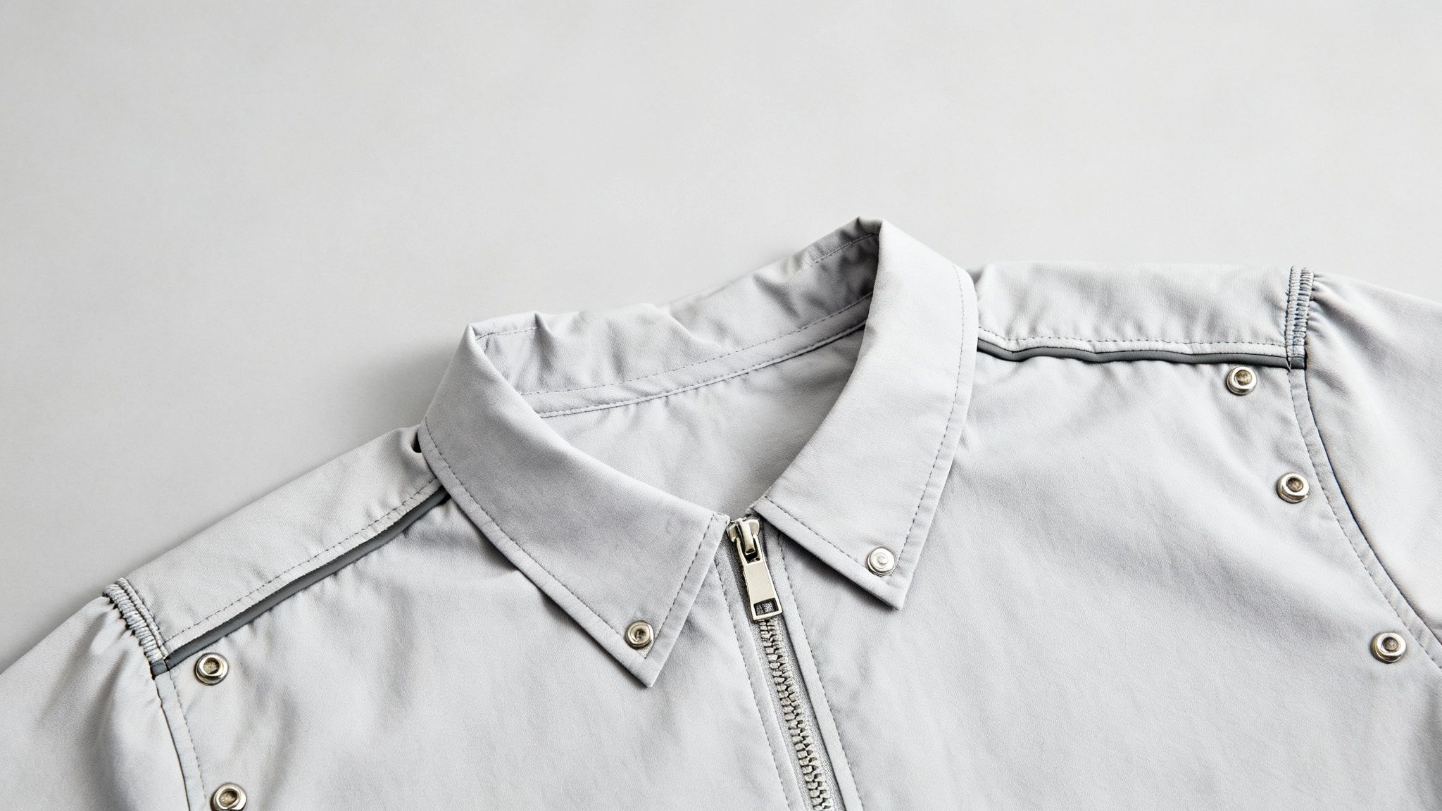 Close-up of a light grey jacket collar featuring a metal zipper and snap buttons.