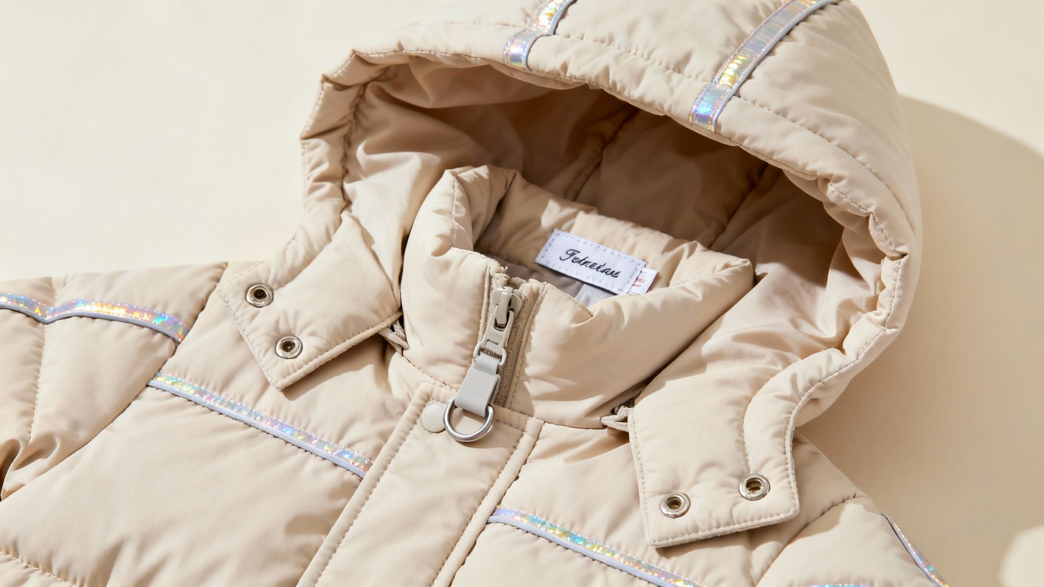 A close-up view of a beige quilted winter coat with a hood and iridescent reflective strips.