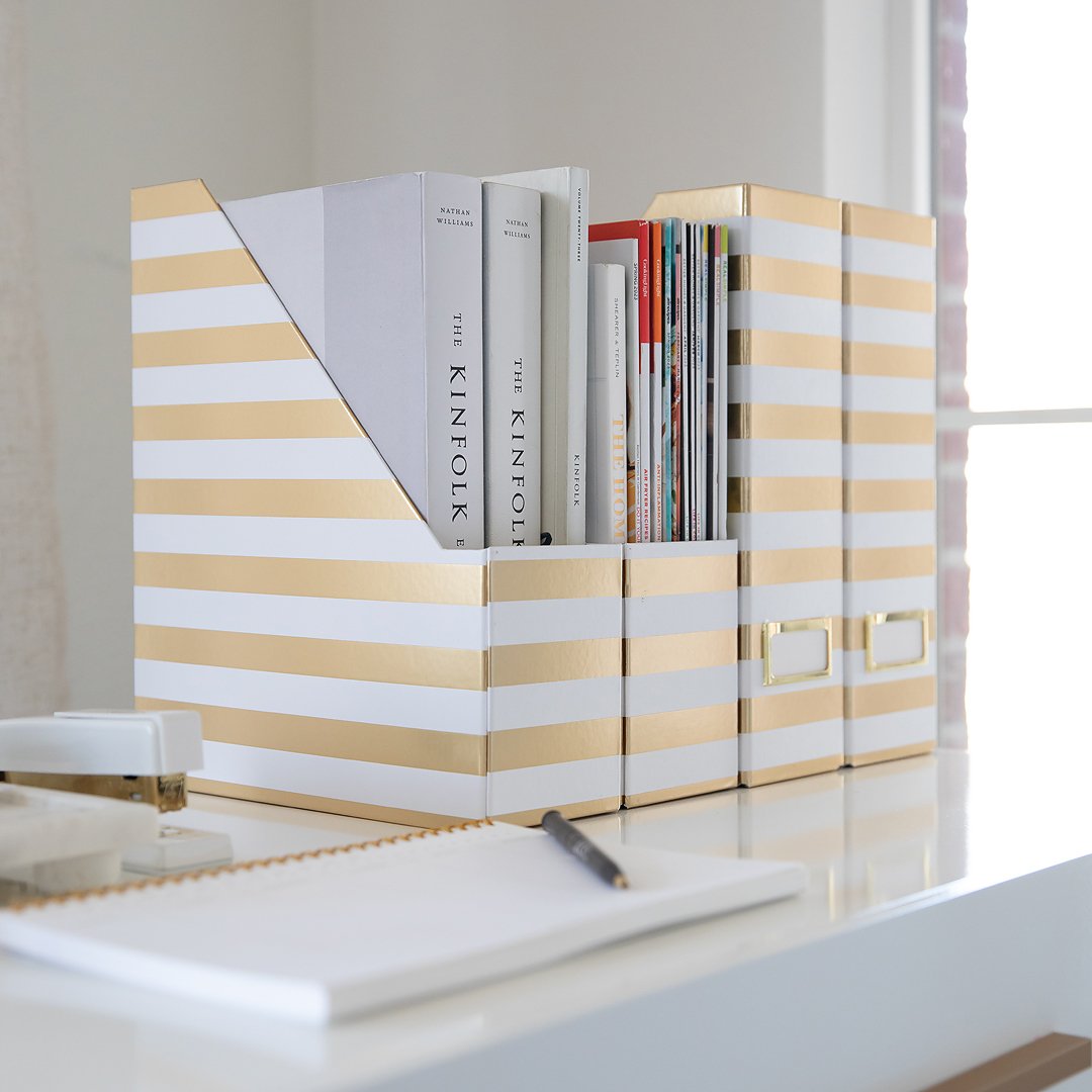 Gold and white striped magazine files and storage boxes neatly arranged on a bright white desk.