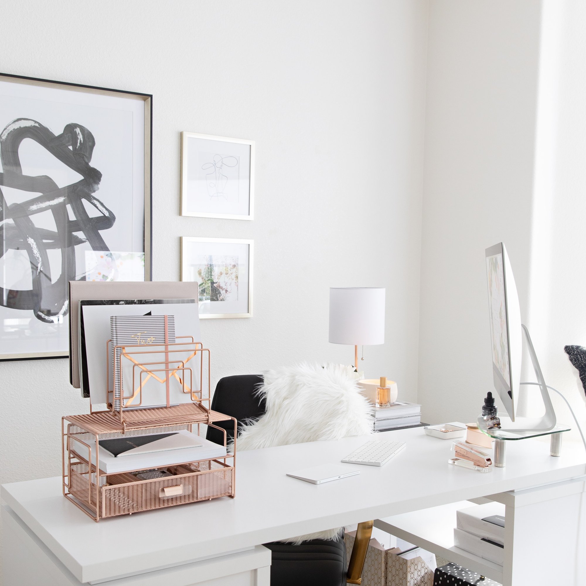 A clean, modern home office setup with a white desk, computer, and rose gold desk organizer.