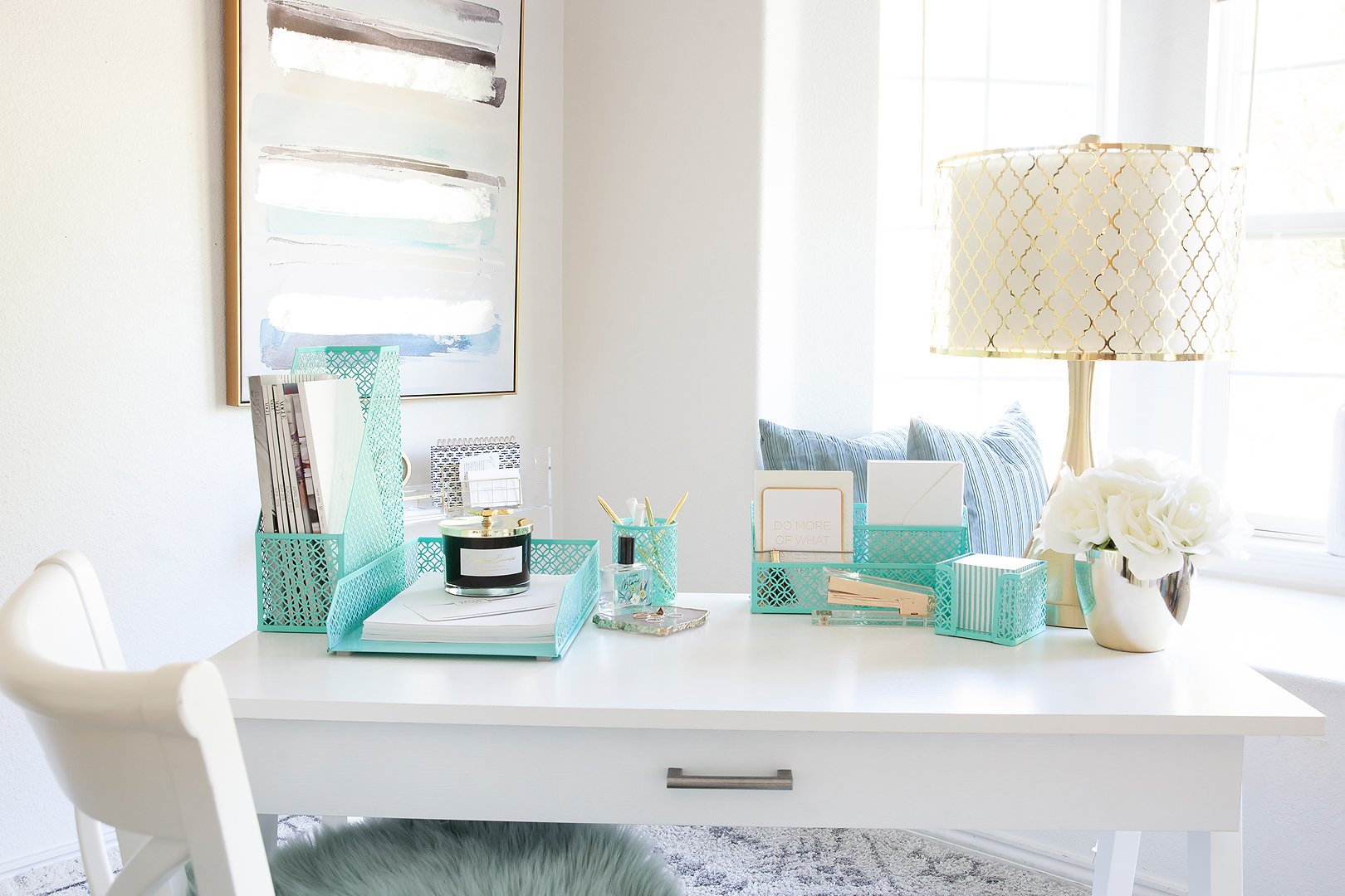 A bright home office desk featuring matching mint green organizers, abstract art, and a decorative lamp.