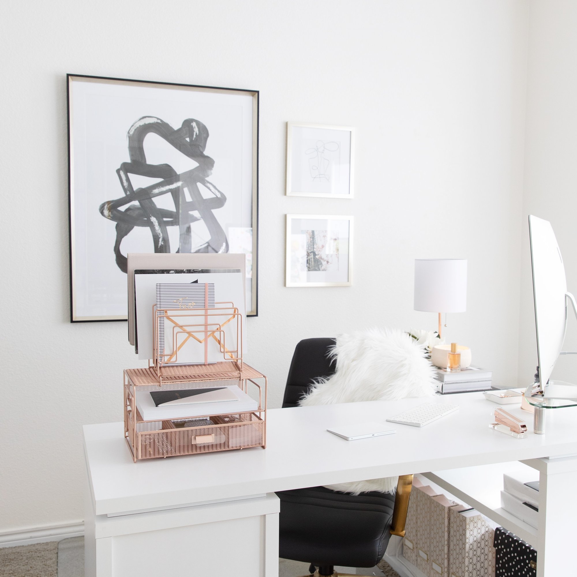 A bright, organized home office featuring a white desk, black chair, and rose gold desk accessories.